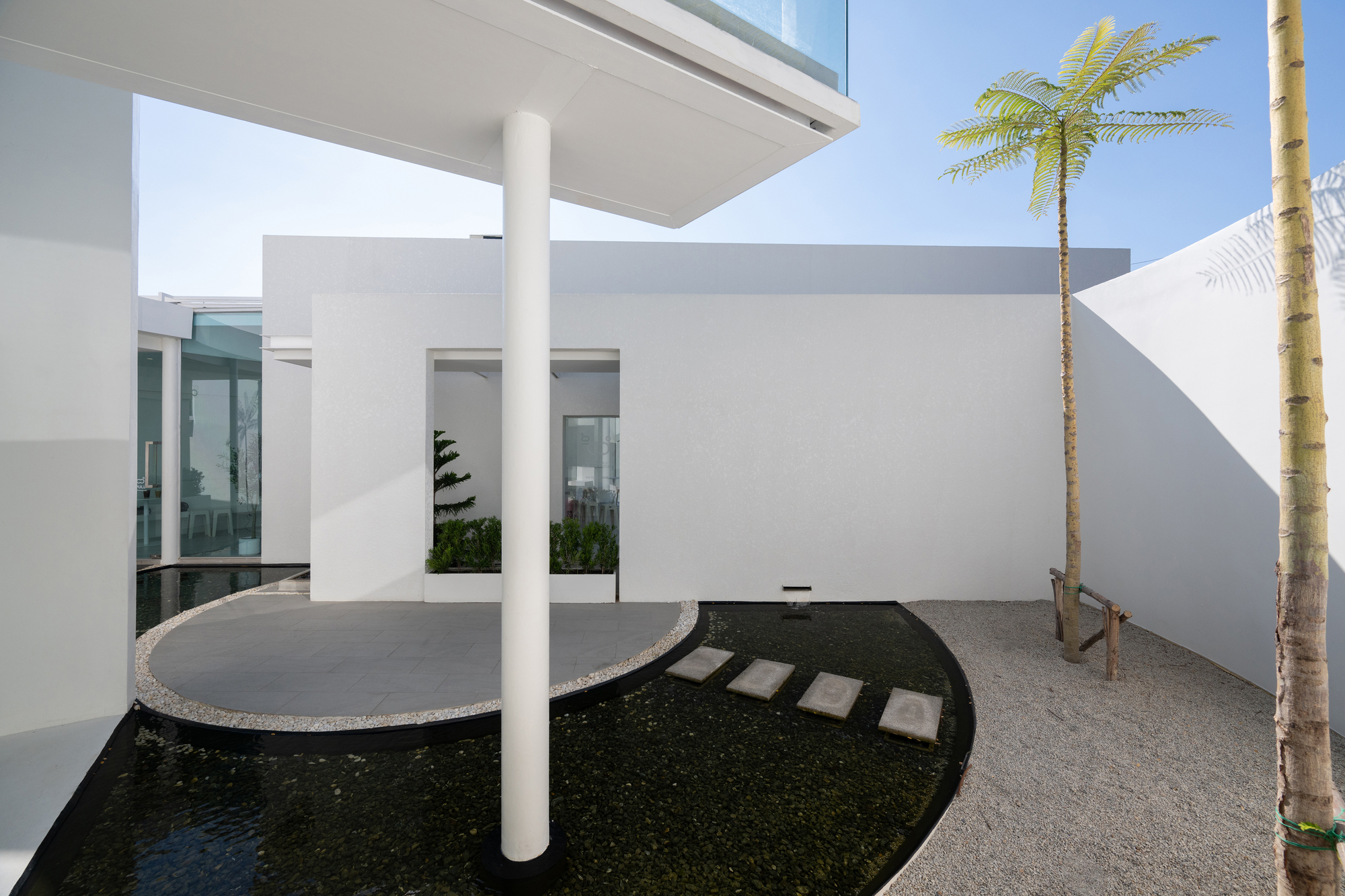 Covered terrace with white columns overlooking a dark reflecting pool with stepping stones