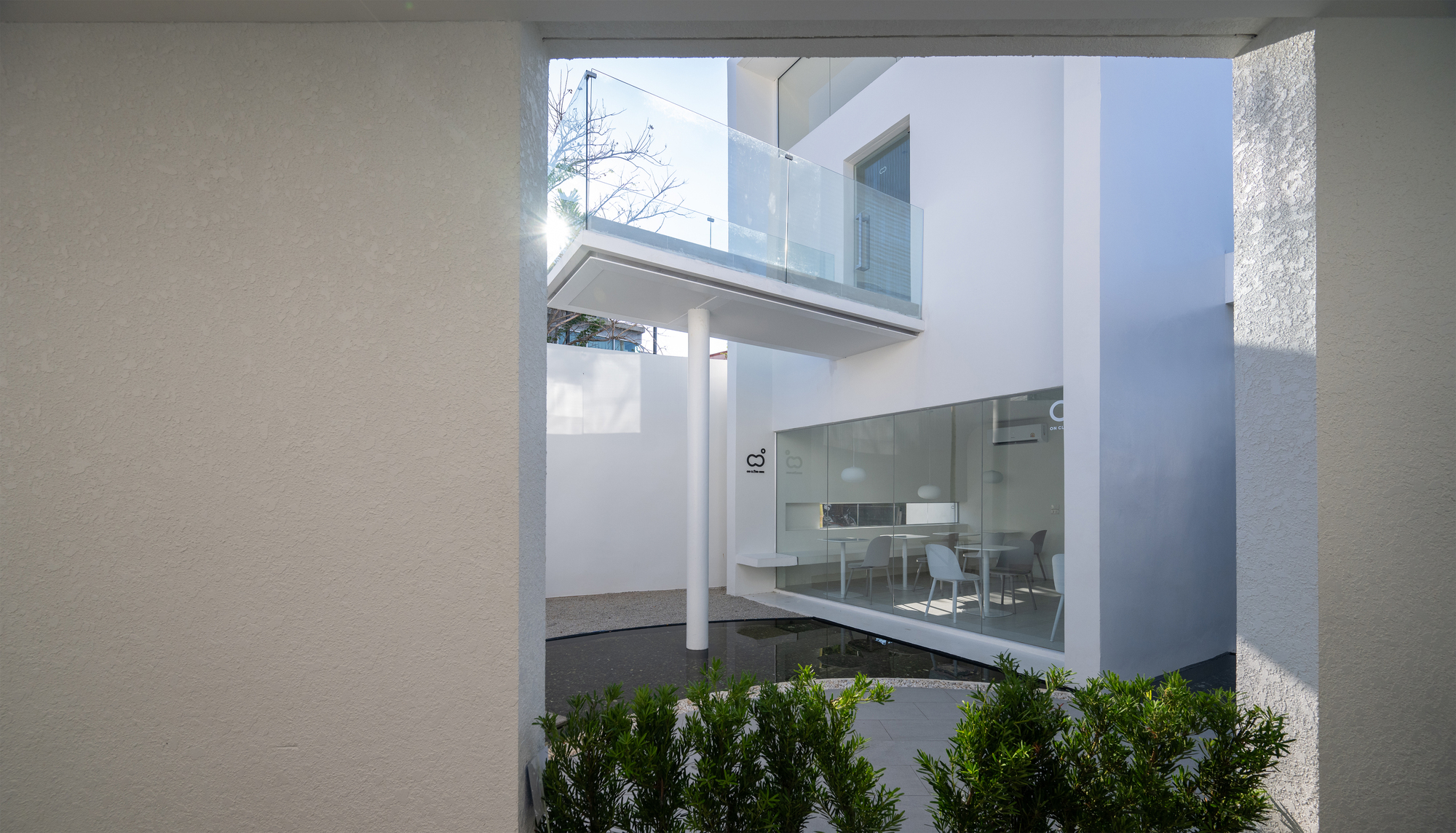 View through opening framing a glass-enclosed dining space across a courtyard