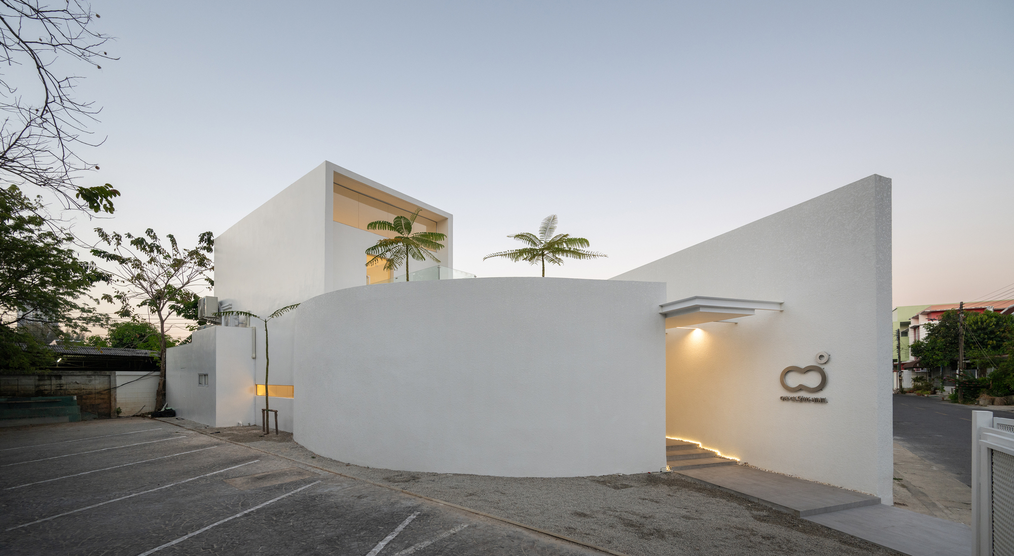 Street-facing facade with curved white stucco wall and recessed entry beneath palm trees at dusk