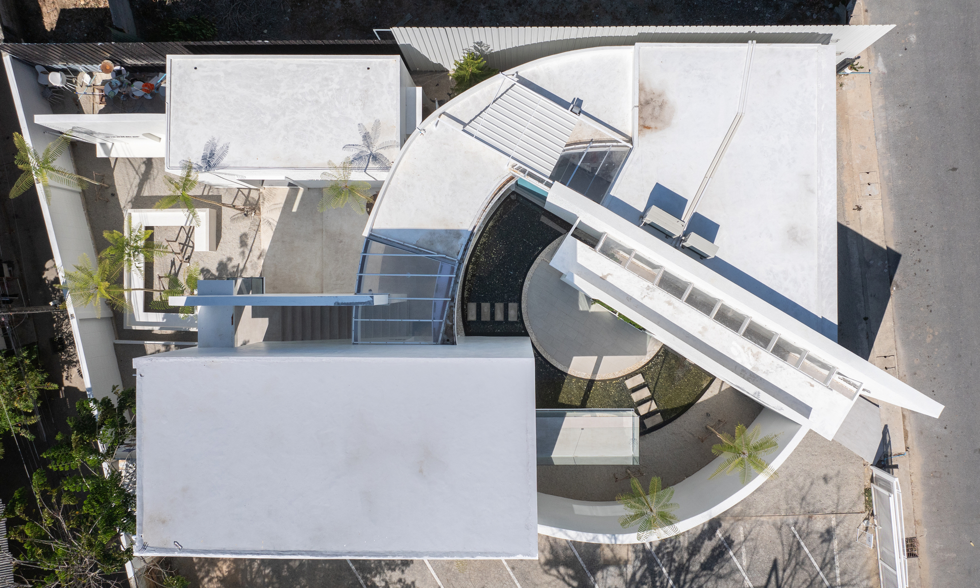 Aerial view of white rooftop with curved canopy, pool and louvered shading elements in bright sunlight