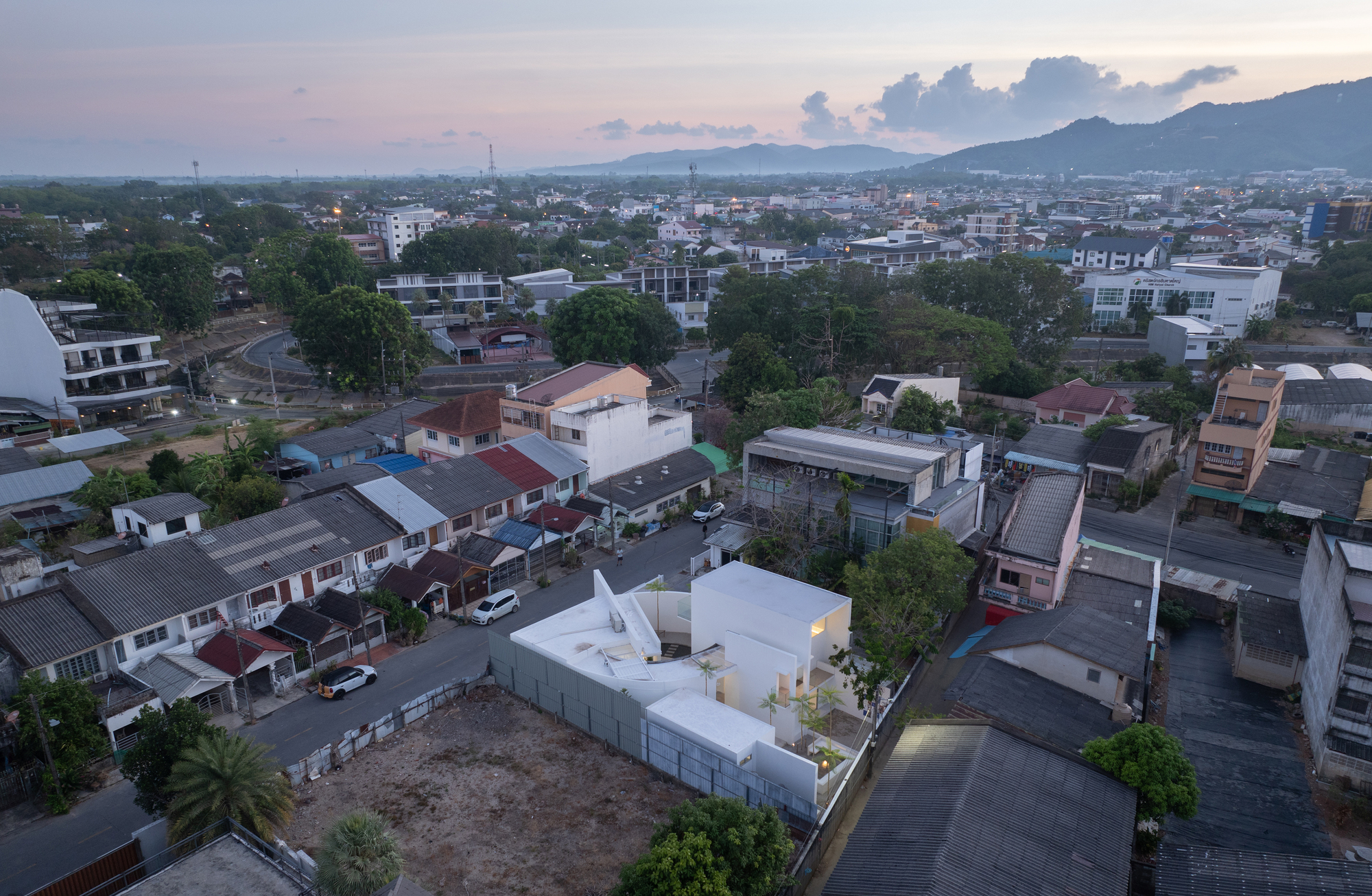 Aerial view of the white angular volumes set within a dense residential neighborhood at dusk