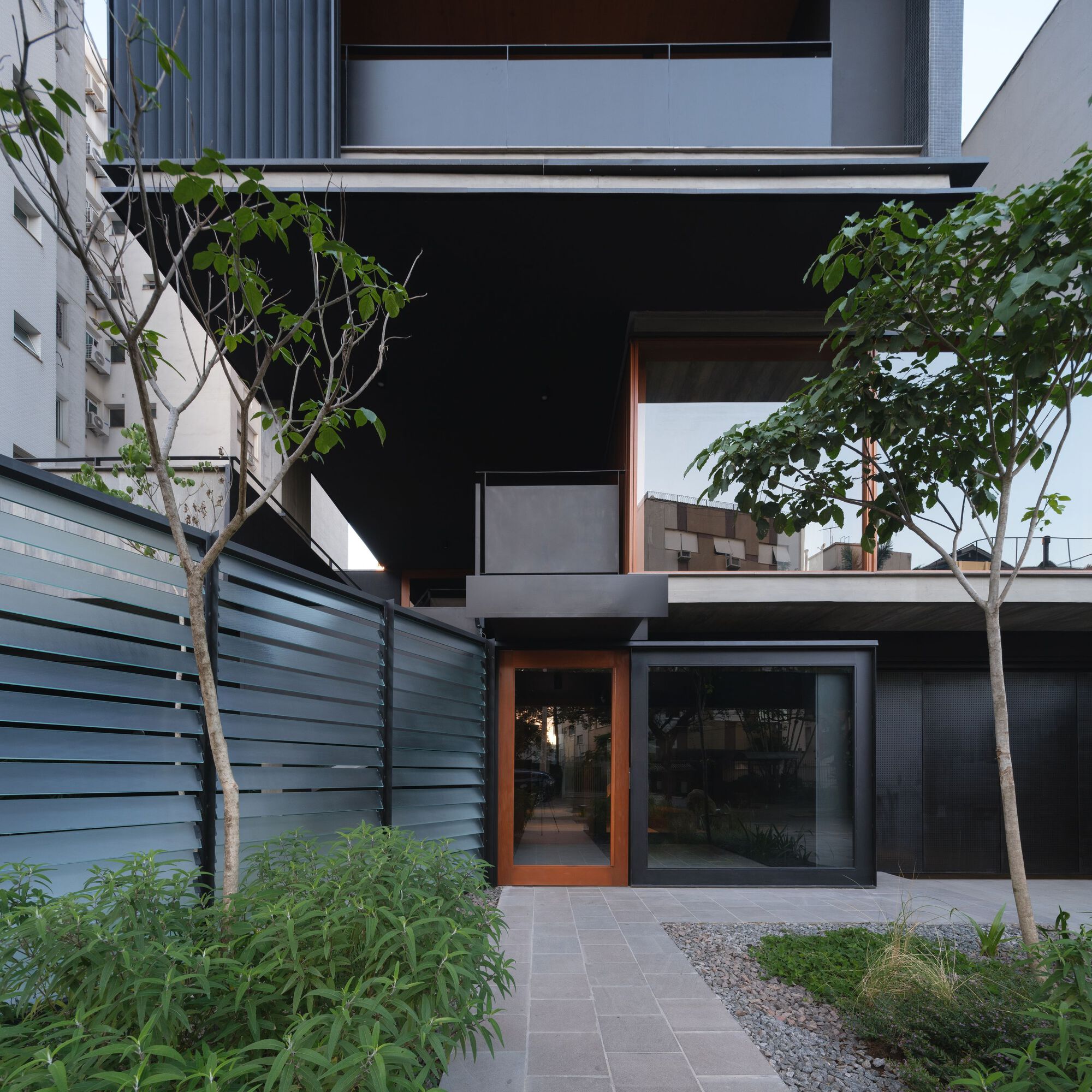 Ground level courtyard with paved tiles, young trees and timber-framed glass doors set in black walls