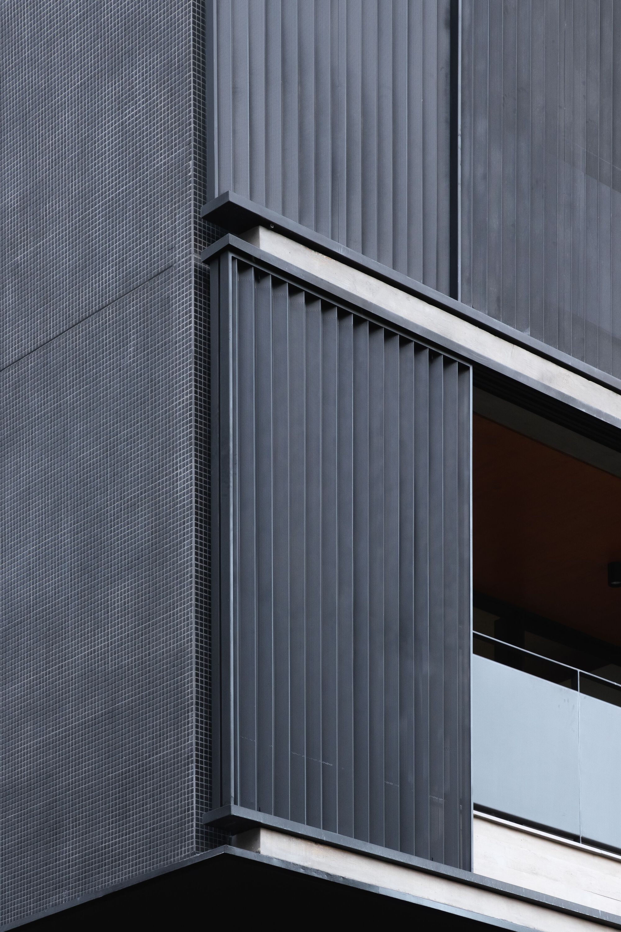 Balcony detail showing vertical corrugated metal screen beside textured grey tile cladding and white guardrail edge