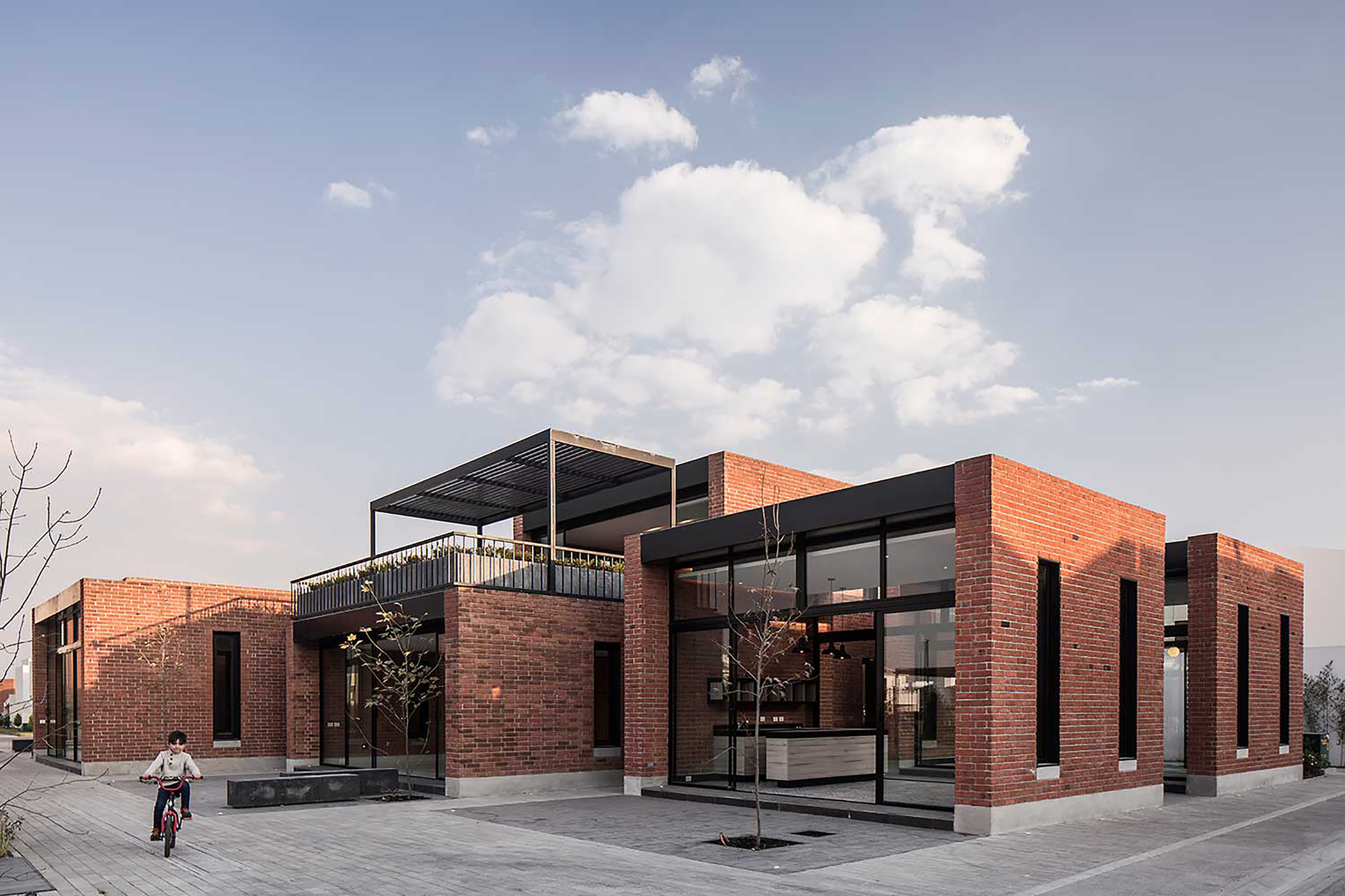 Brick courtyard buildings with black window frames and a rooftop pergola as a child rides a bicycle past