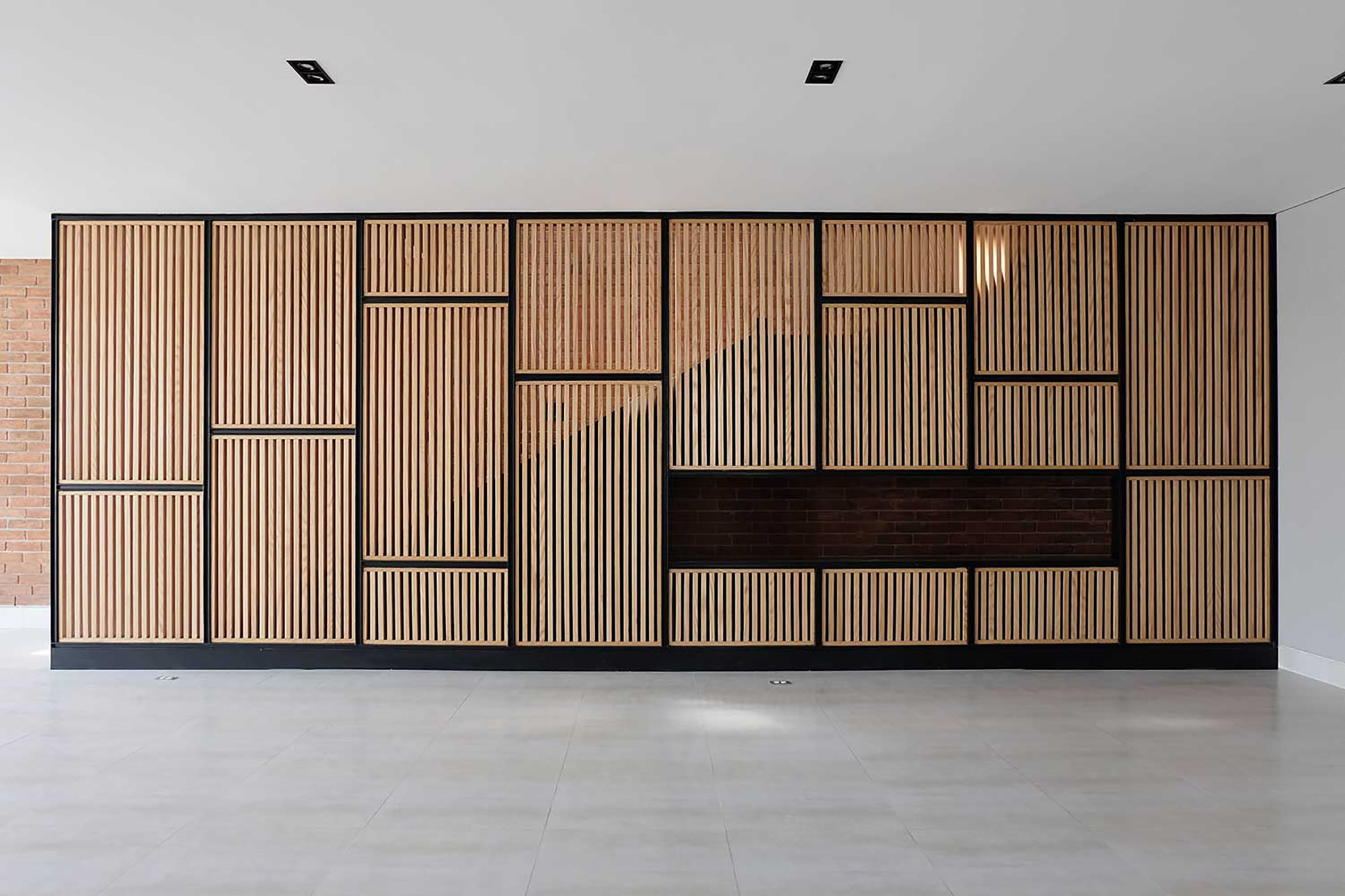 Interior wall of timber slat panels in a black steel grid with a recessed brick niche, sunlight cast across the slats