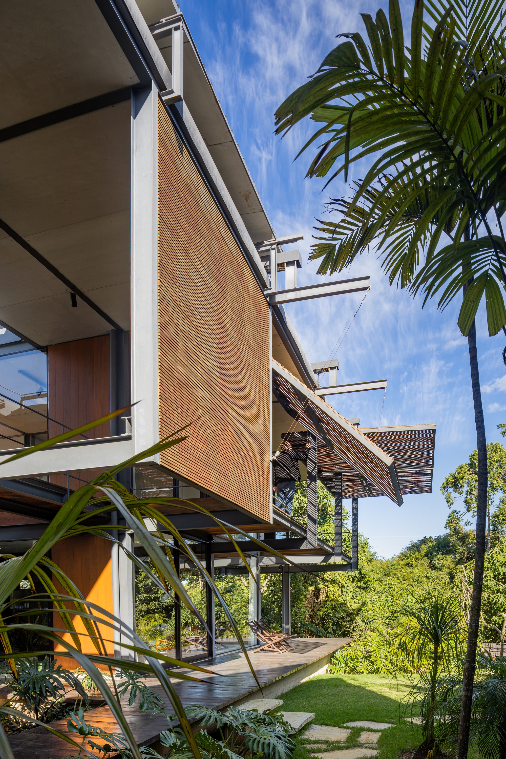 Vertical timber slat screen on the steel frame beside a palm, with the canopy tilting out under a blue sky