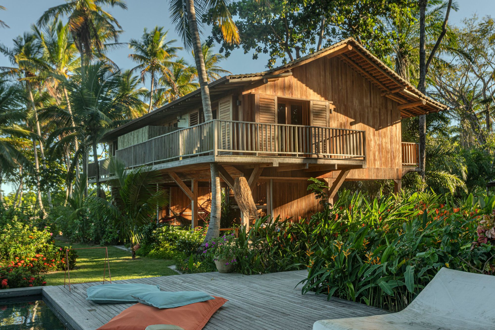 Raised timber house with a railed balcony and shuttered doors above a weathered deck, lit by low golden sunlight