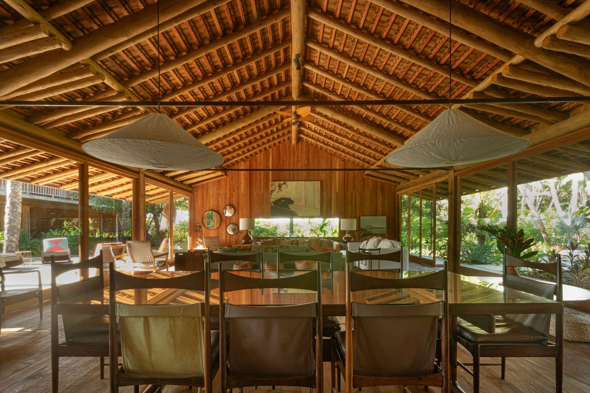 Open dining pavilion with a round-pole rafter roof, a long table with leather chairs and two pendant lamps in daylight