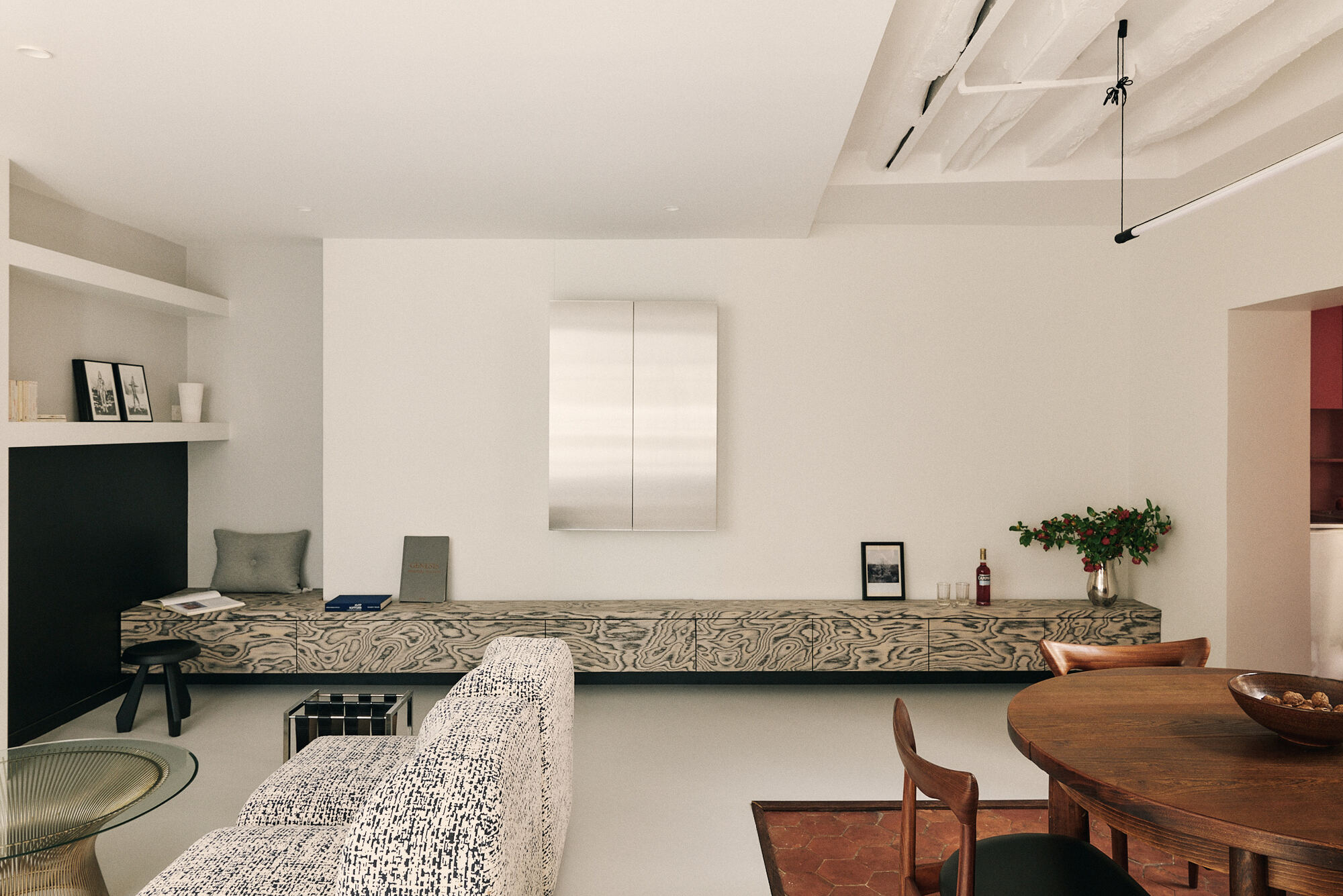 Living room with a floating burl-veneer bench below a steel cabinet, a boucle sofa in front and a dining table at right in soft daylight