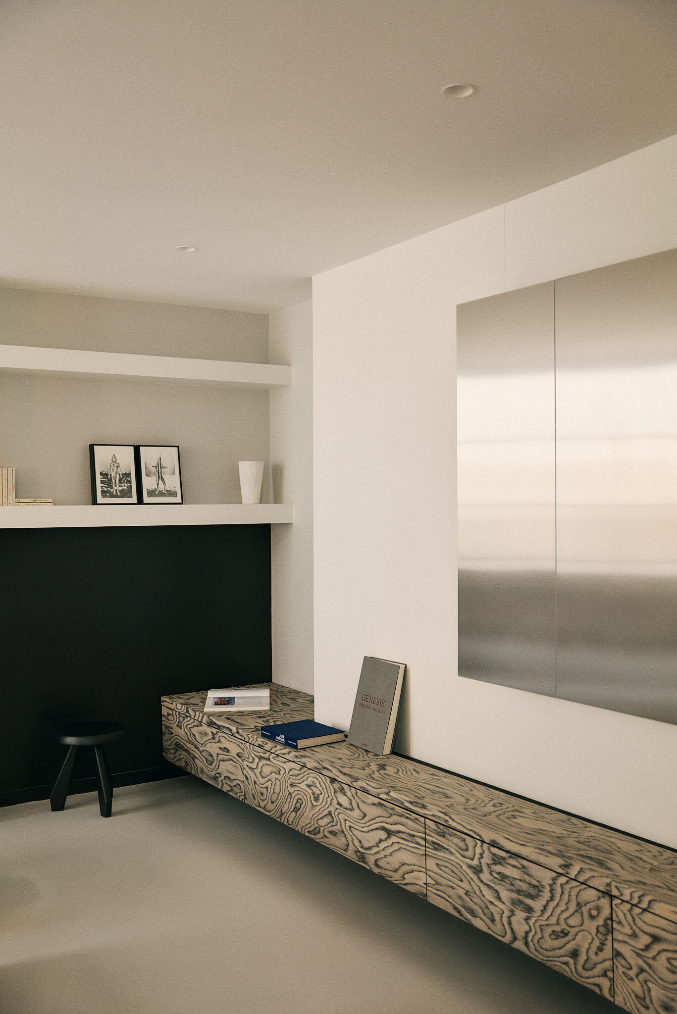 Floating swirl-grain wood bench with books and a stool, set against a brushed steel panel and black niche in soft diffused light