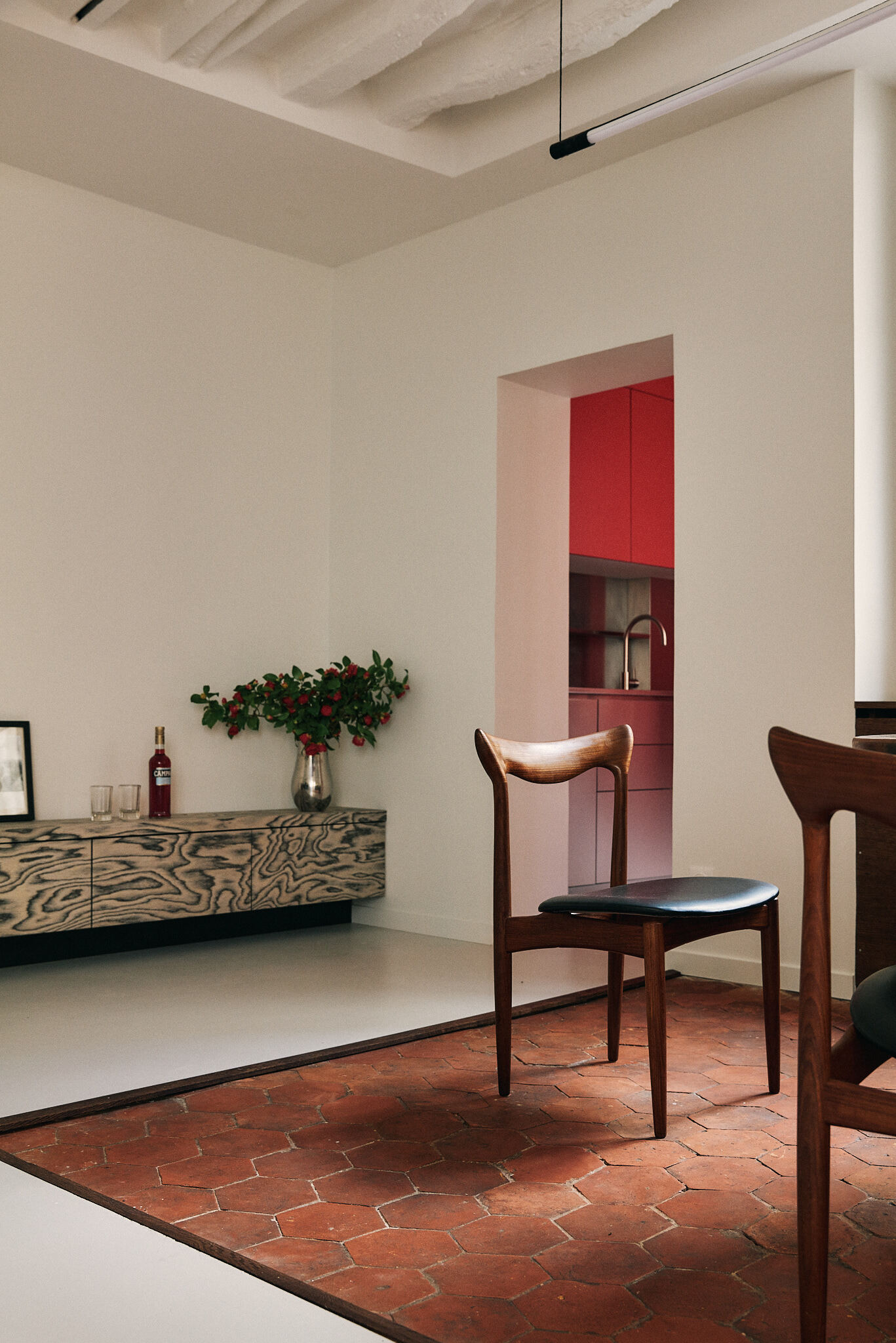 Teak chair on a hexagonal terracotta tile inset, with the wood-grain sideboard and a red kitchen glimpsed through a doorway
