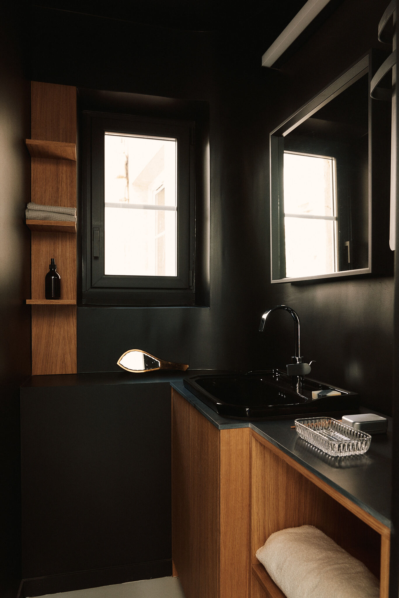 Compact washroom with a black basin, oak shelving and a small window glowing with afternoon light