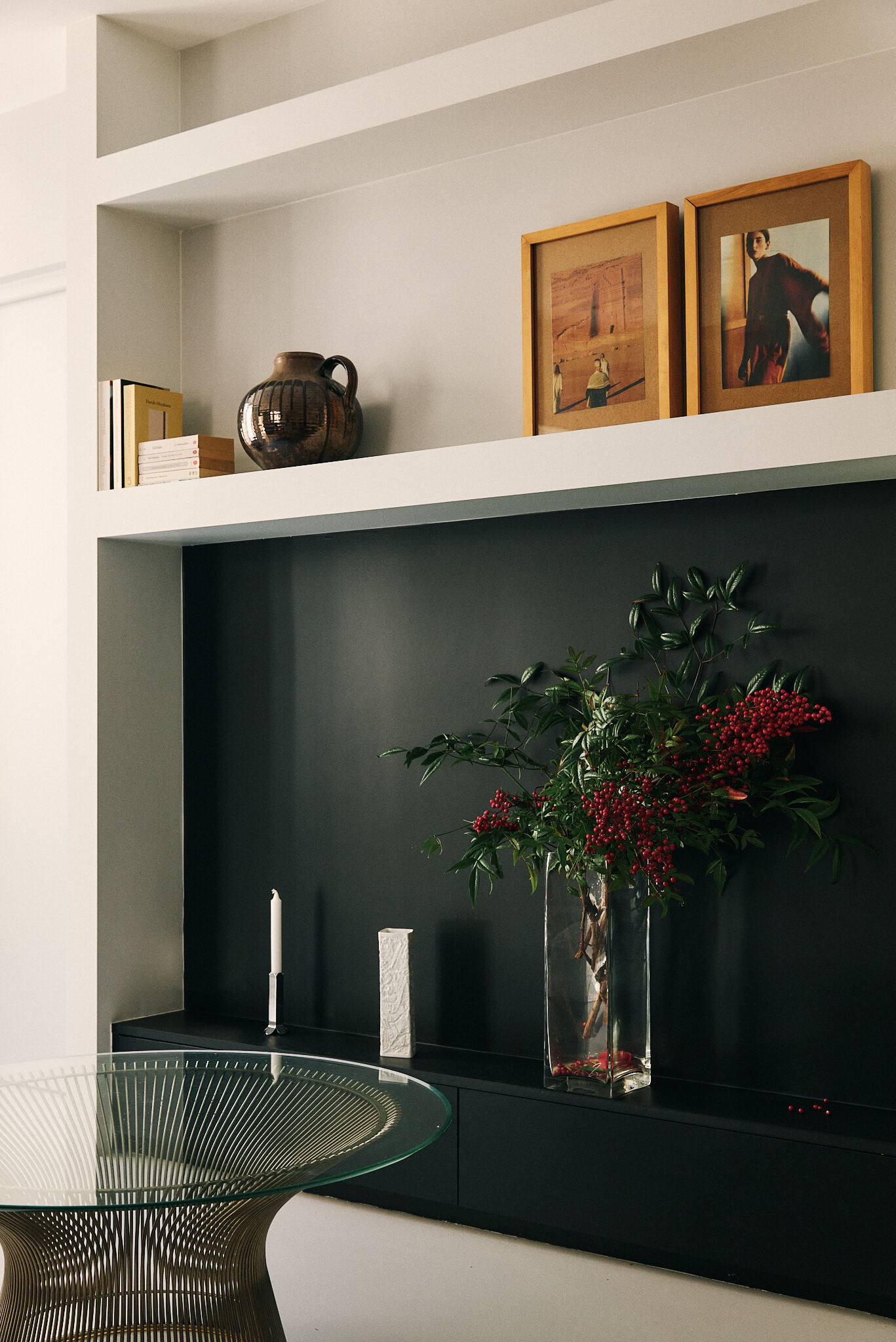 Recessed shelf above a black credenza, with framed prints, a ceramic jug and red berry branches in a glass vase