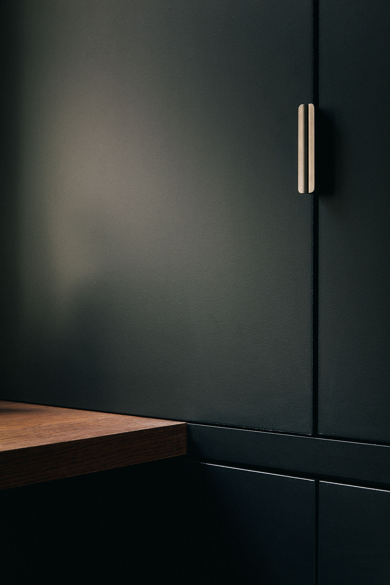 Close-up of a brass pull on a matte black cabinet door beside the edge of a walnut desktop