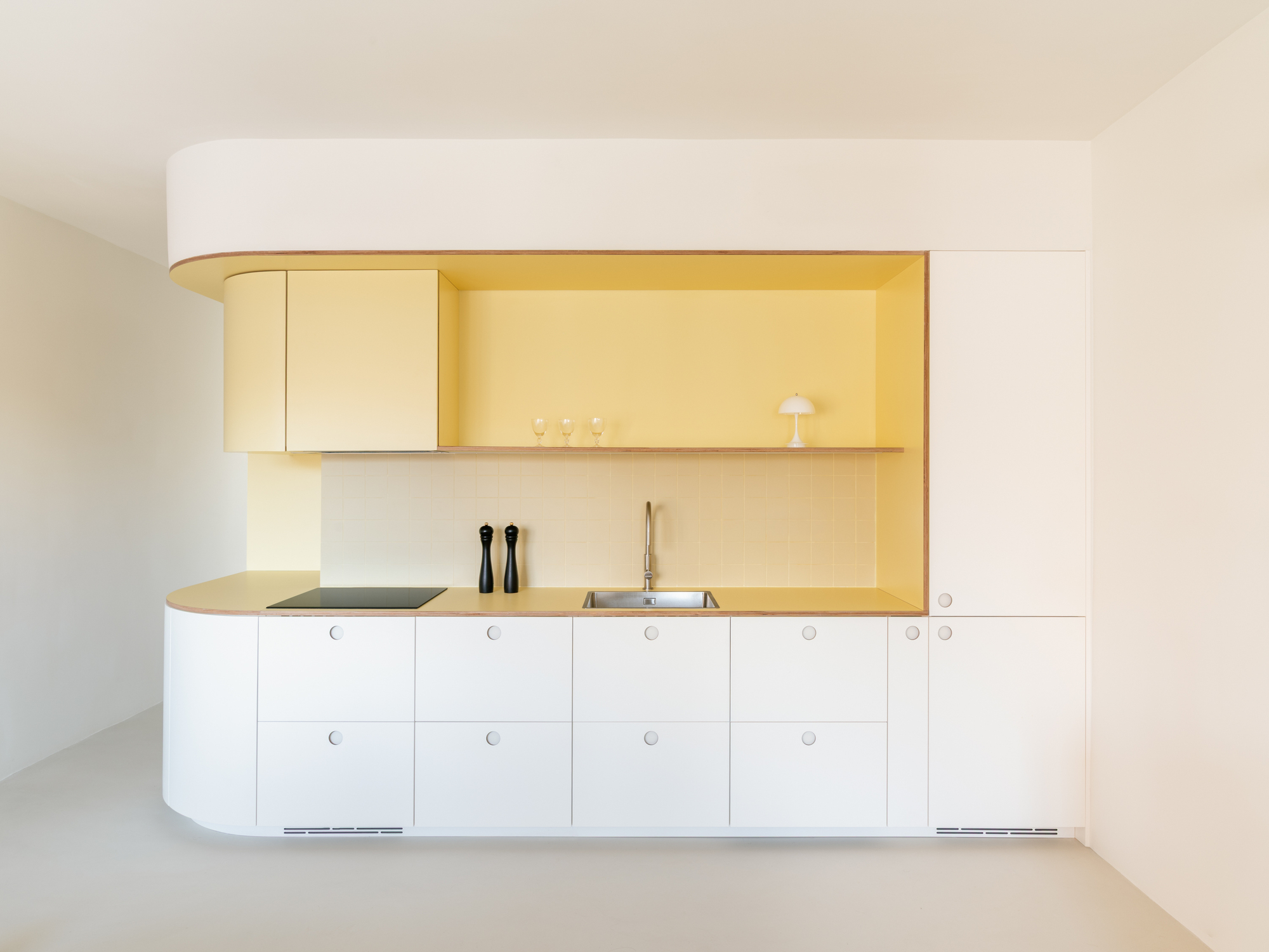 Frontal view of a white kitchen run with a rounded end and a pale yellow recess, lit by soft daylight