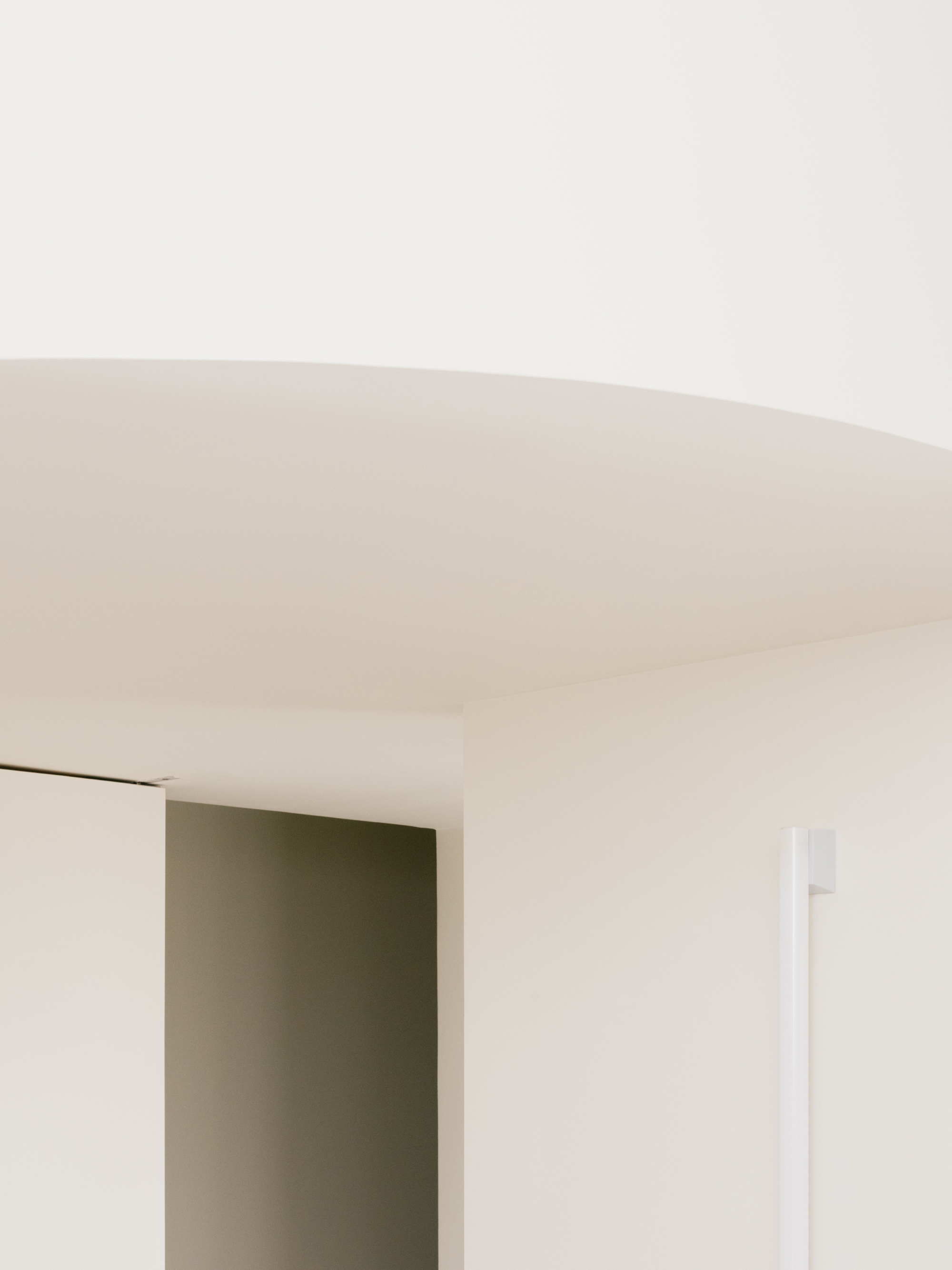 Curved white soffit above a recessed doorway and a slim vertical handle in diffuse daylight