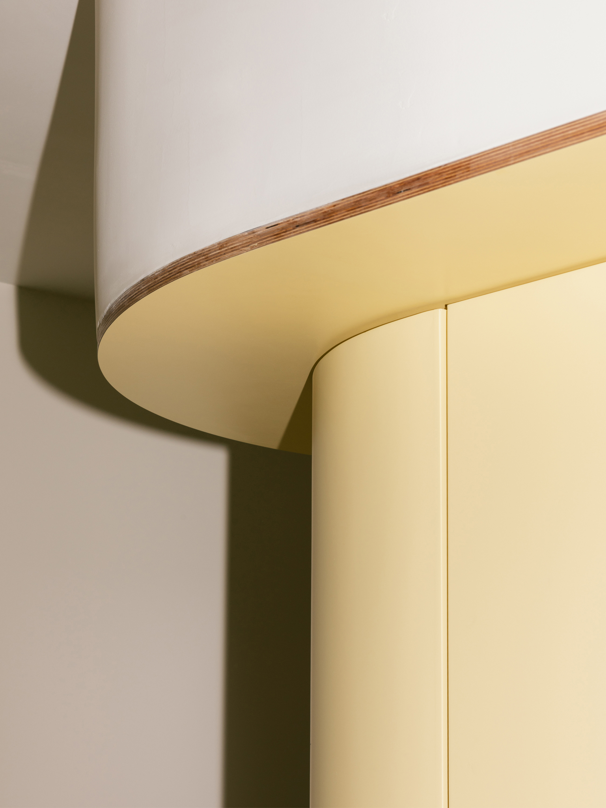 Close-up of a rounded plywood edge where a white cabinet top meets pale yellow curved doors