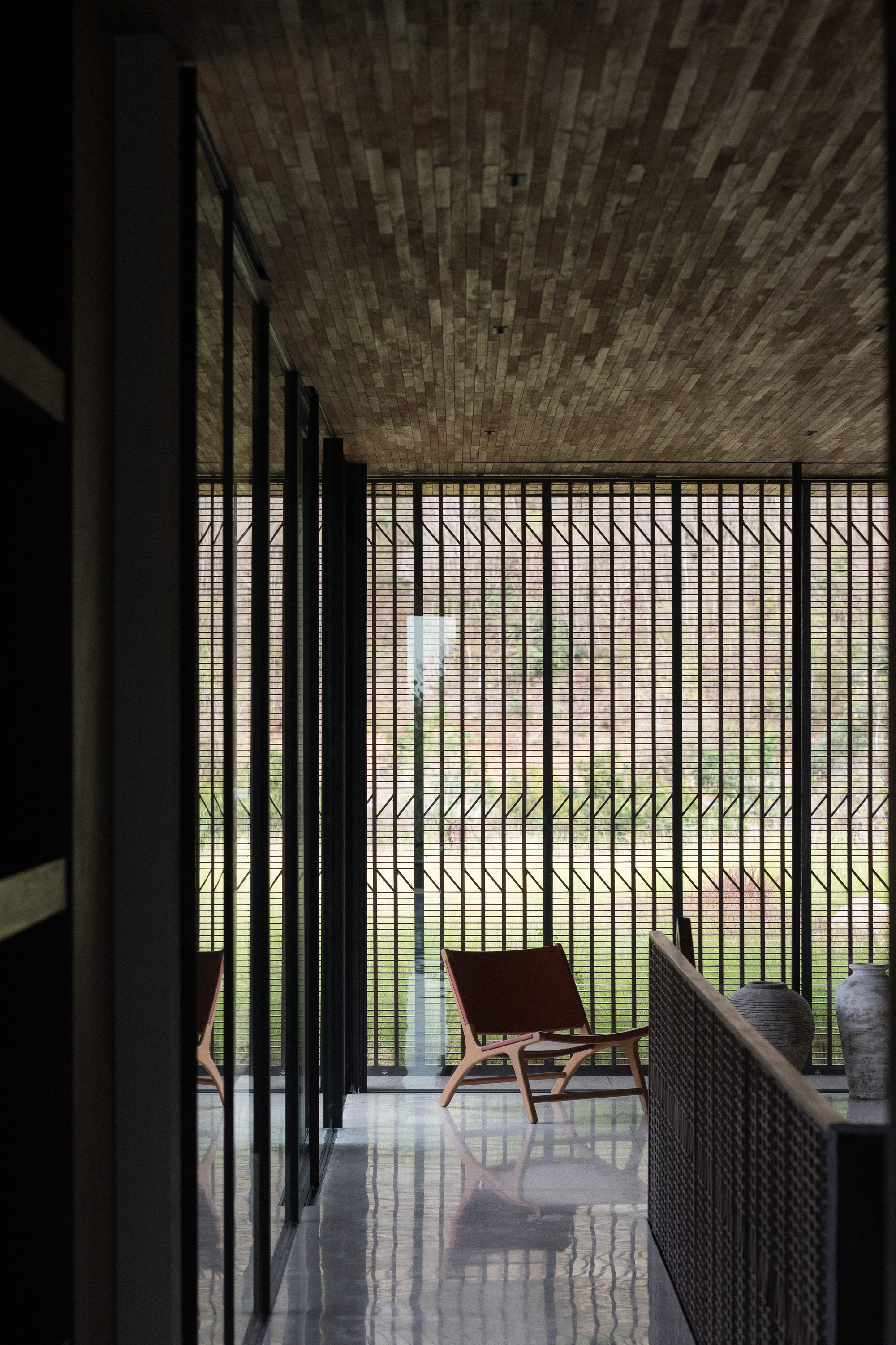 Upper hallway with a brick-pattern timber ceiling, black steel screen and a leather chair beside ceramic jars in soft daylight