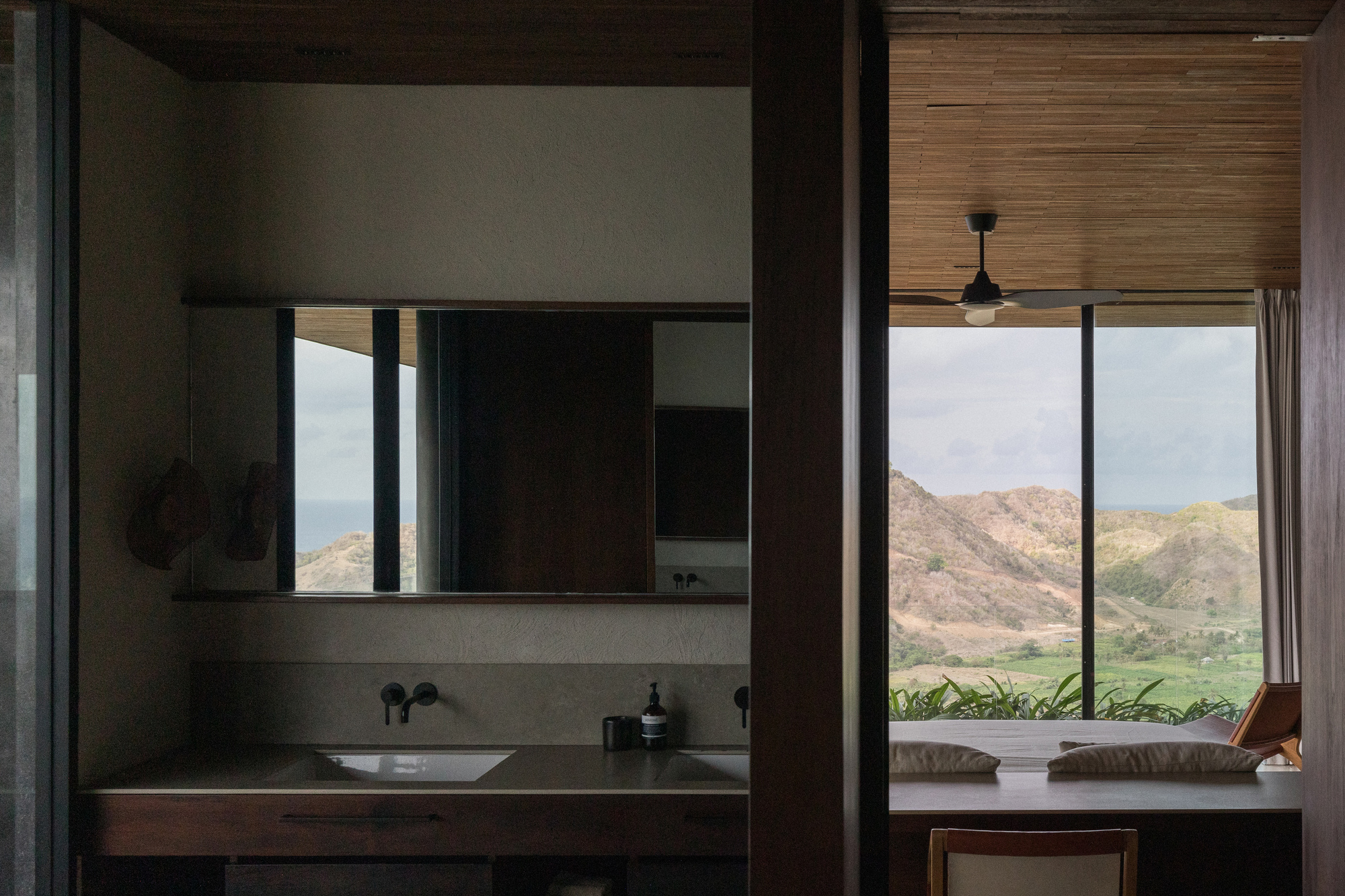 Bathroom vanity with wall-mounted taps and mirror beside a daybed window that looks out to dry hills under cloud
