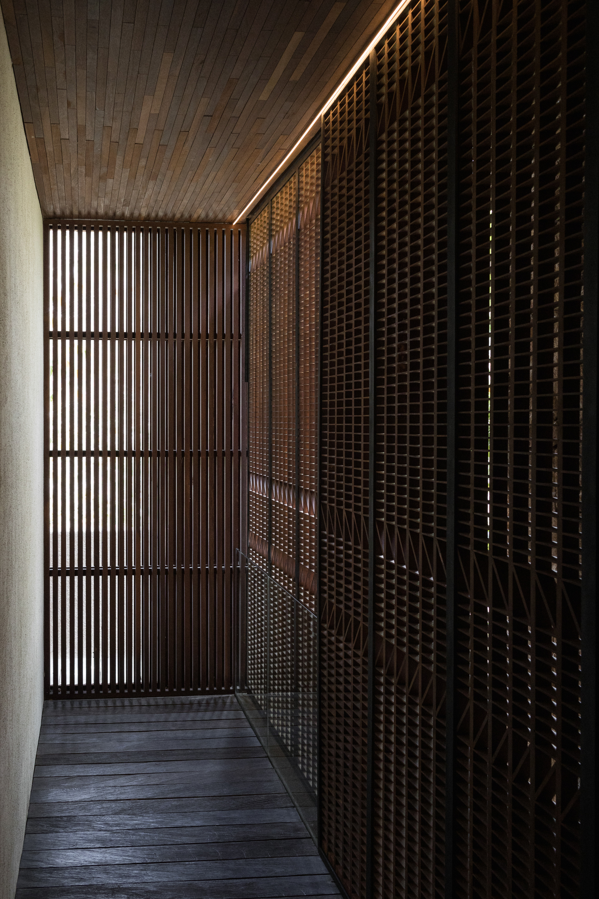 Narrow timber-floored passage lined with dark metal lattice screens and a lit strip along the wooden ceiling