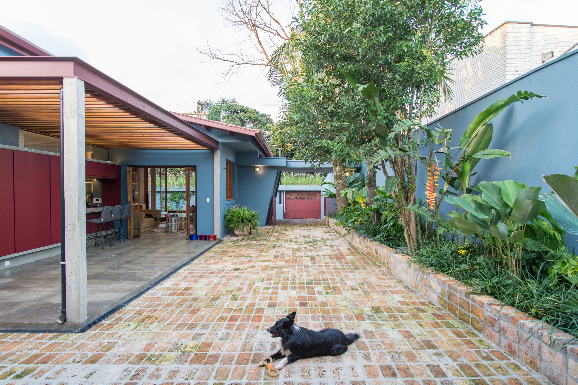 Reclaimed brick courtyard with a black dog resting beside a planted bed, a concrete column and open timber-framed doors