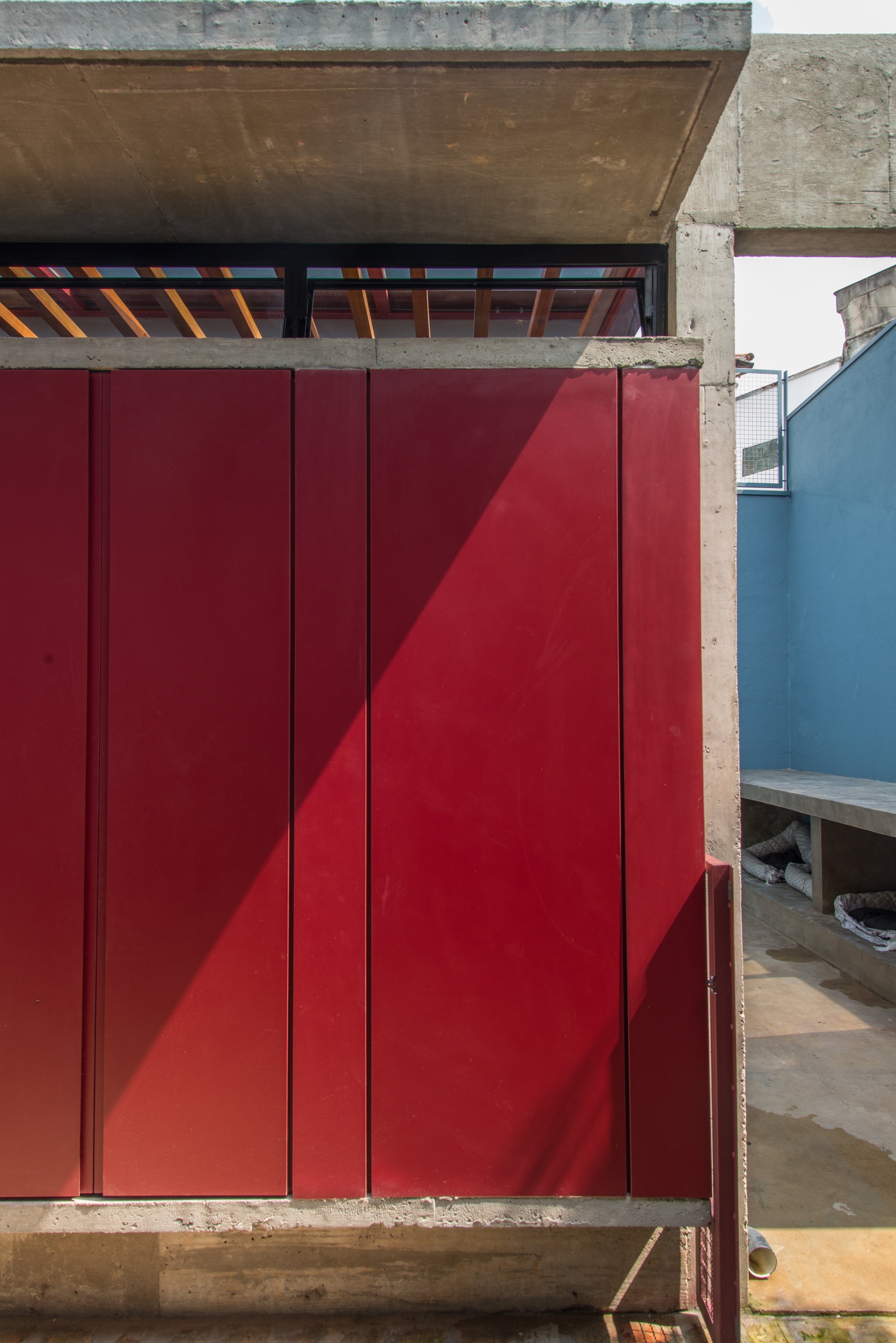Close-up of red vertical wall panels beneath a concrete slab, with diagonal sunlight cutting across them