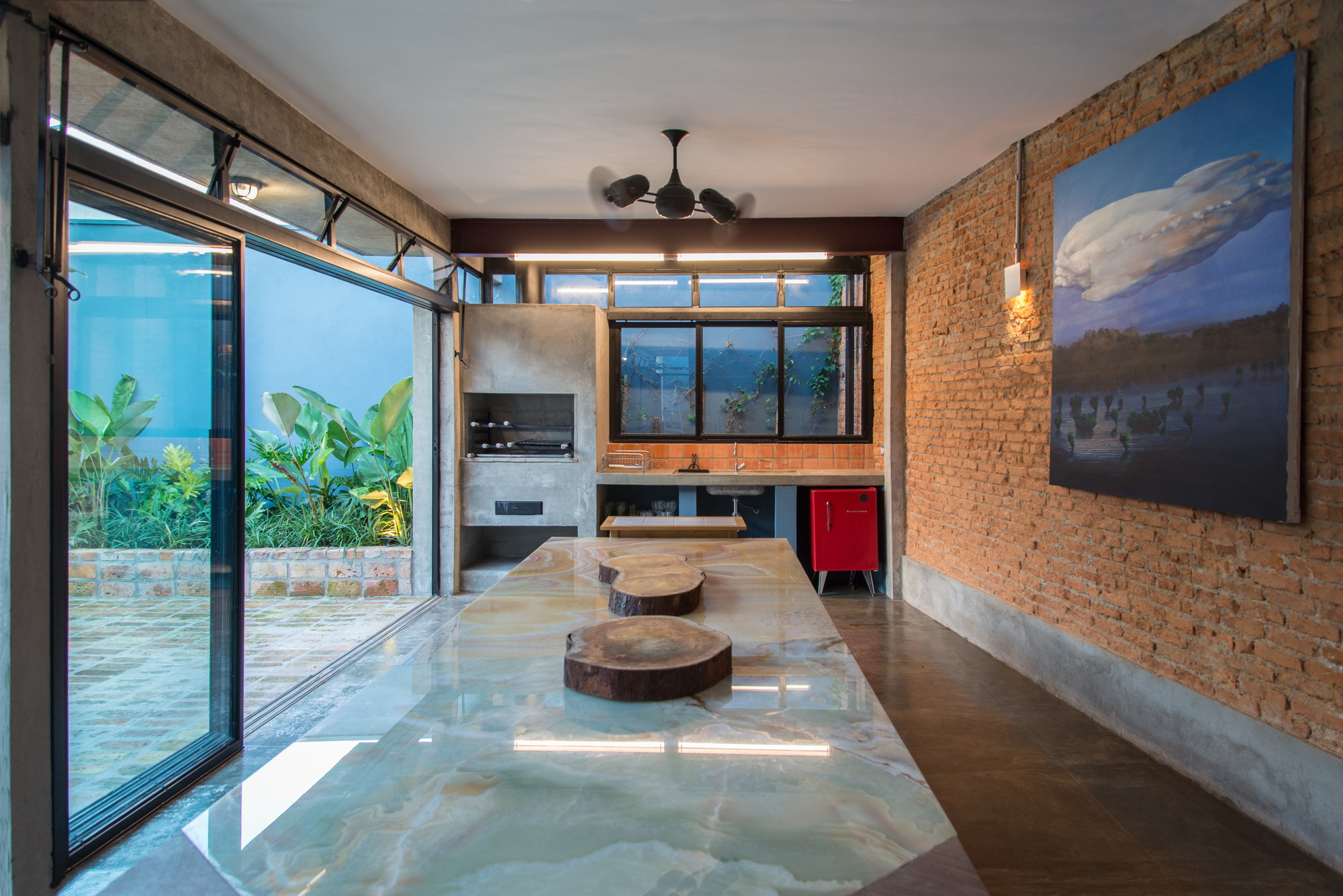 Kitchen with a long green onyx island, built-in grill and exposed brick wall, opening through glass doors to a planted court