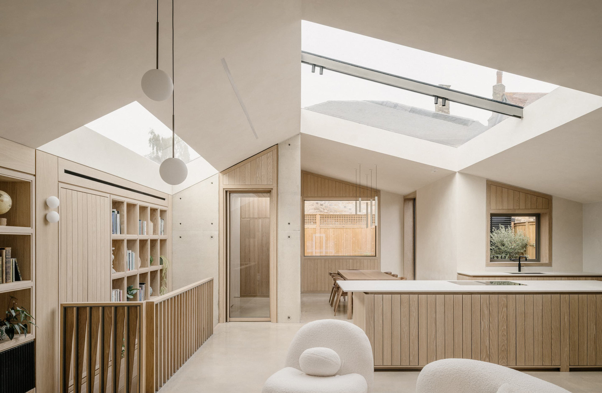 Open living space with angled rooflights, oak joinery and a slatted balustrade, lit by soft overcast daylight