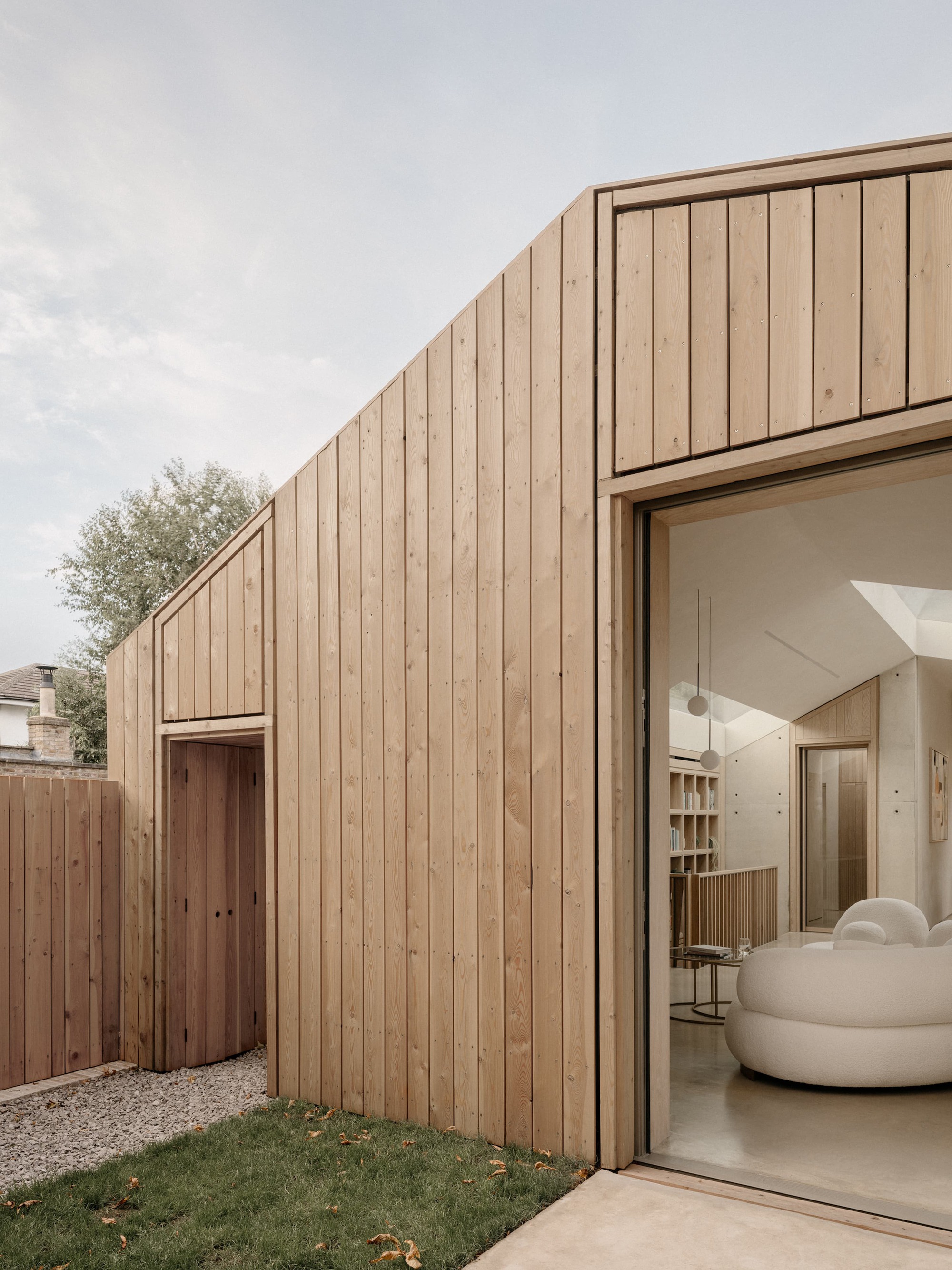 Vertical timber cladding on a gabled garden facade with a glazed opening onto the living room, beside a lawn with fallen leaves