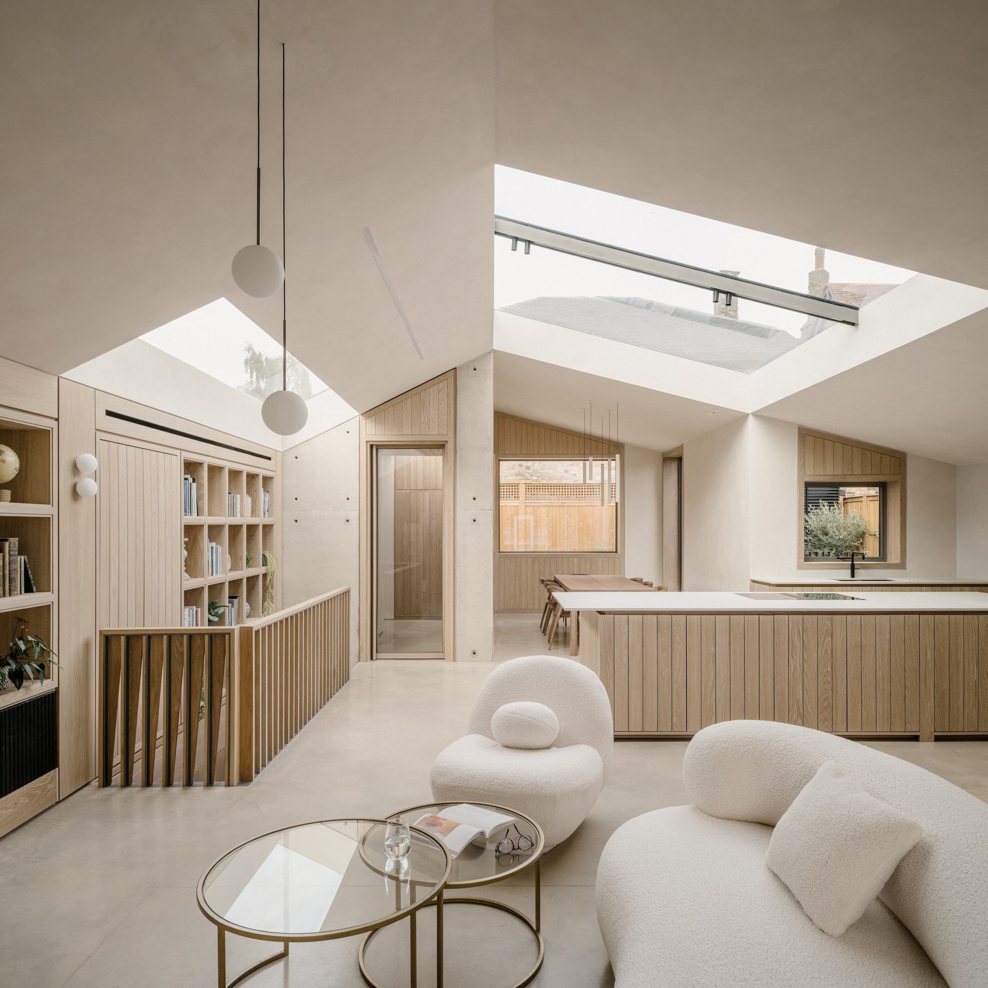 Living area with boucle seating and brass coffee tables, facing an oak kitchen island under large angled rooflights