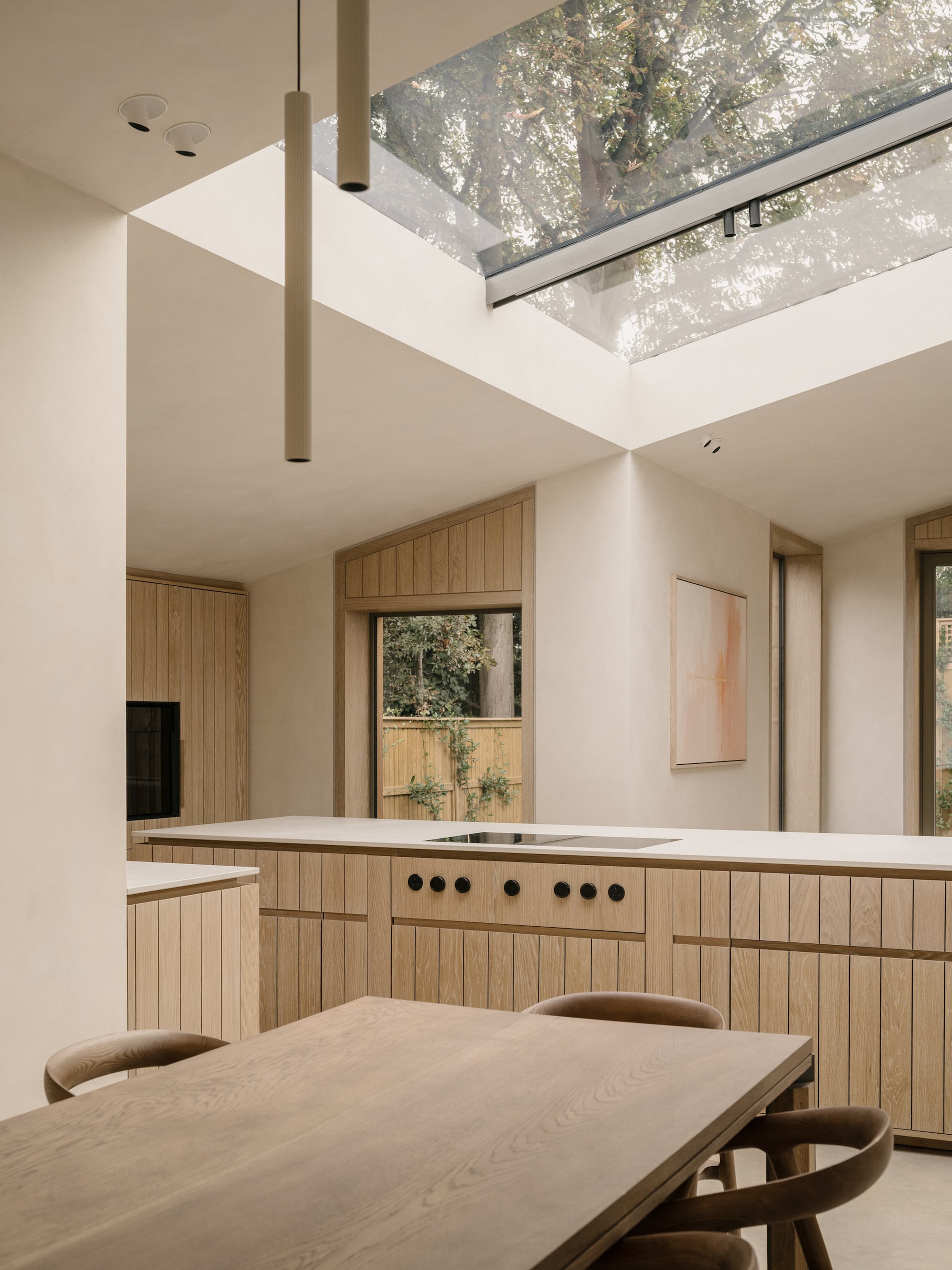 Kitchen with oak-fronted island and induction hob beneath a large angled rooflight, with tree canopy visible through the glass