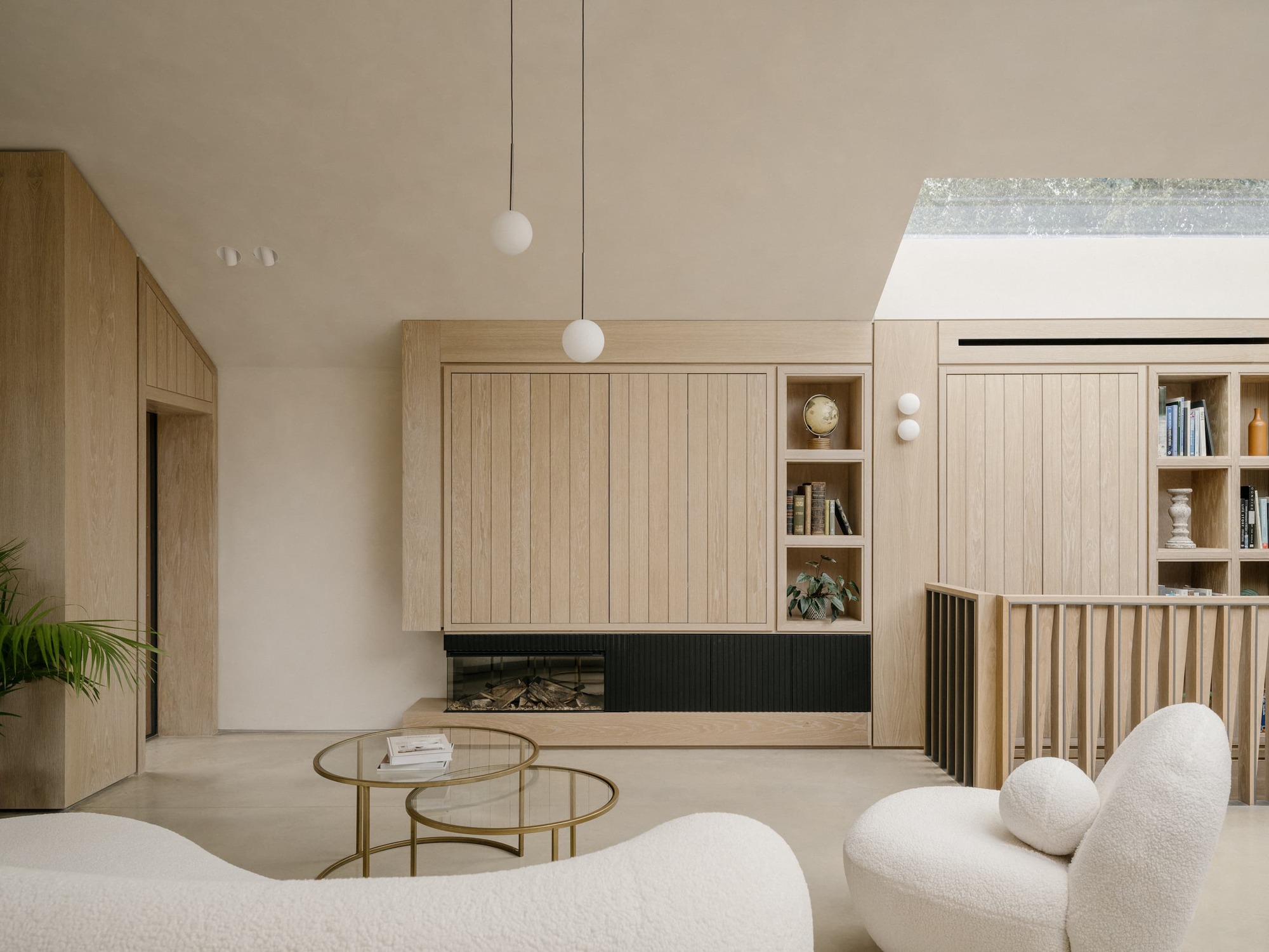 Living area with oak panelled storage wall, inset fireplace and bookshelves, bouclé seating in the foreground and daylight from a rooflight