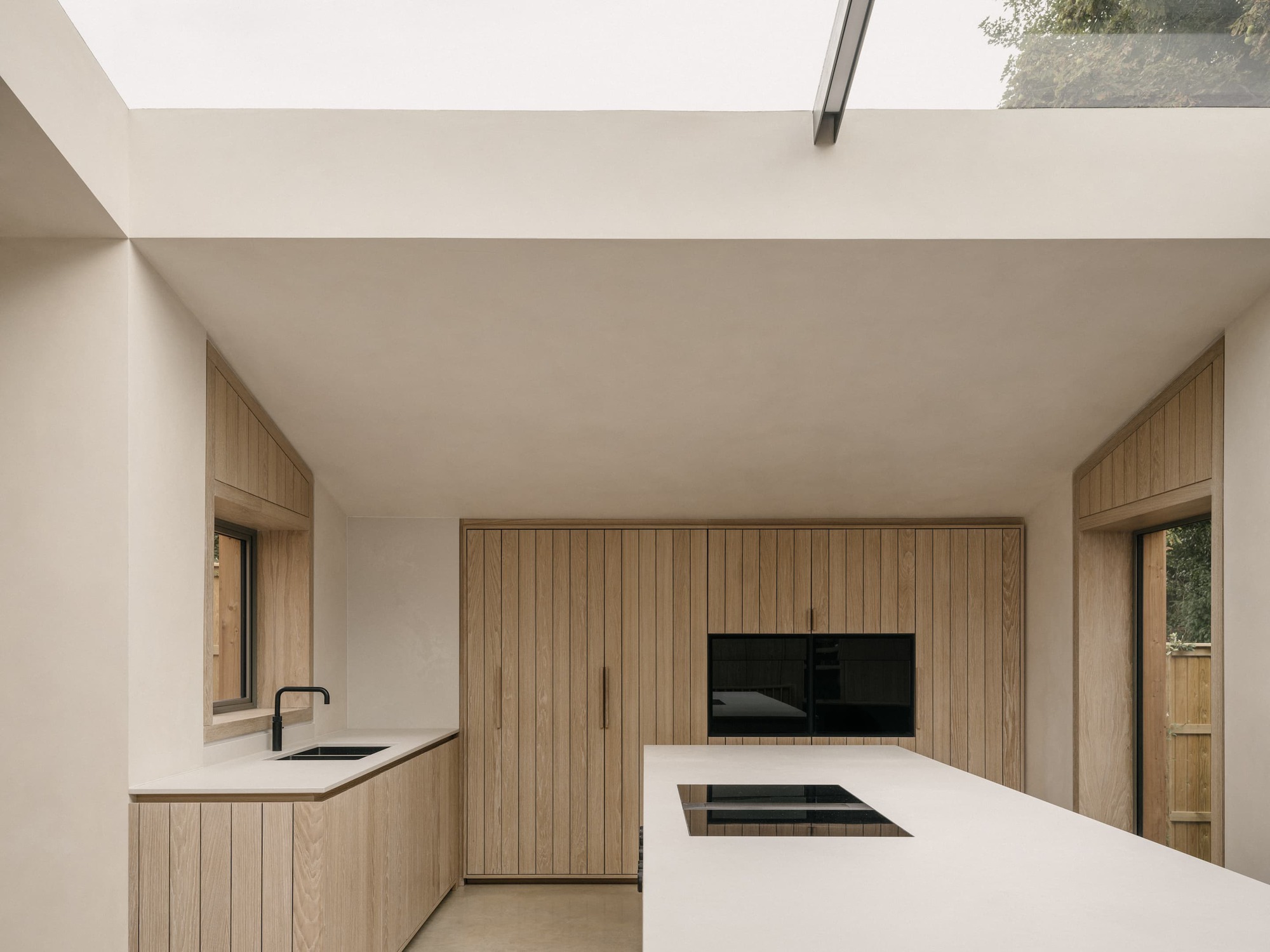 Kitchen with oak cabinetry, pale stone island with induction hob and a large rooflight admitting overcast daylight and tree views