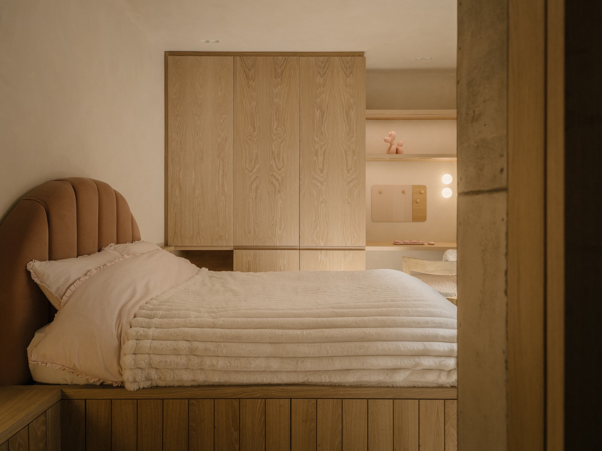 Child's bed with a scalloped rust headboard on a timber platform, set against oak wardrobes in warm evening light