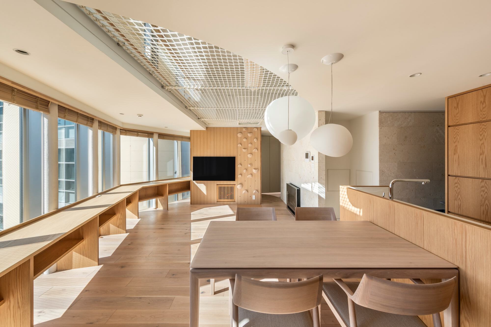 Open living and dining room with oak joinery, a long window bench and a rope net ceiling in afternoon sun