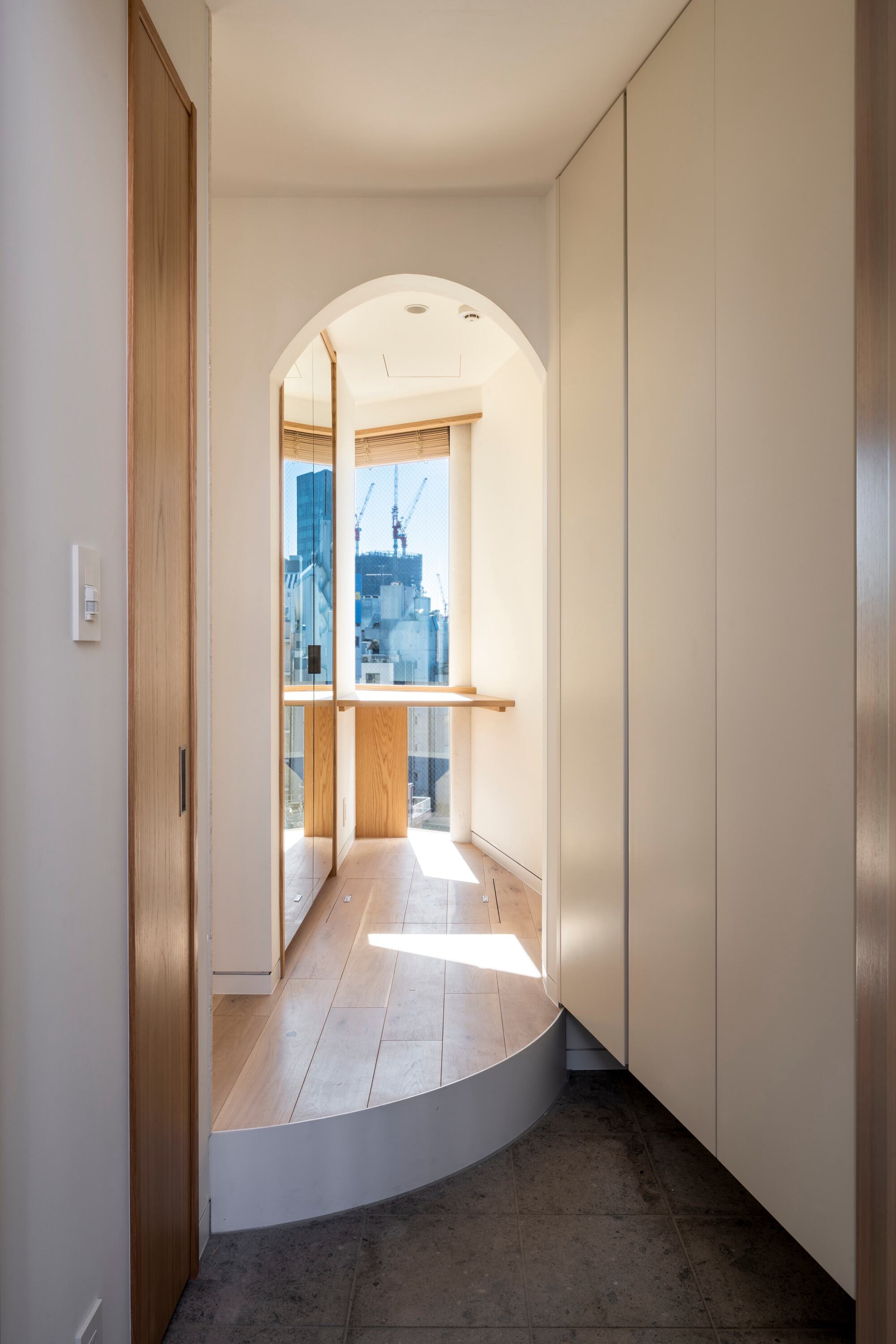 Arched alcove with a timber shelf at the end of an entry hall, a curved step and sunlight on the floor