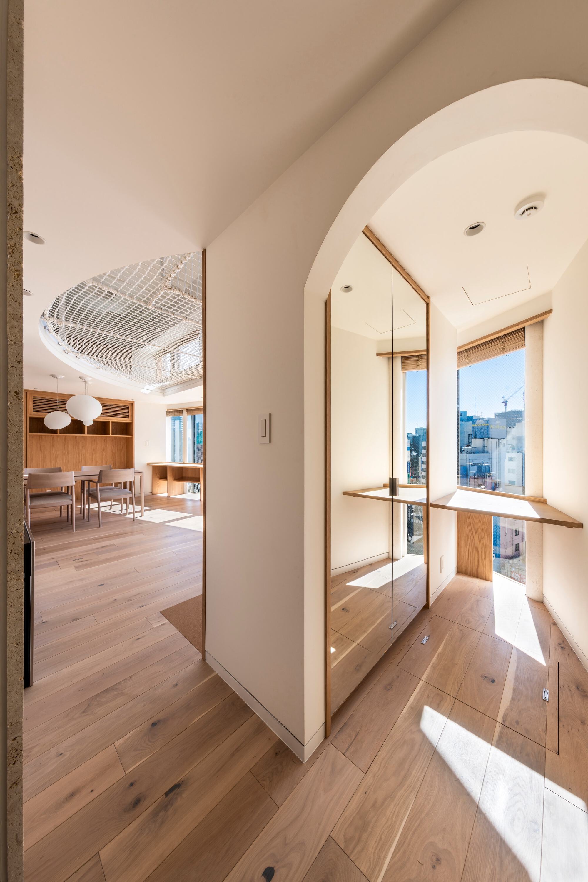 Arched window nook with a wood sill and mirrored panel, opening toward a dining area with a netted ceiling opening