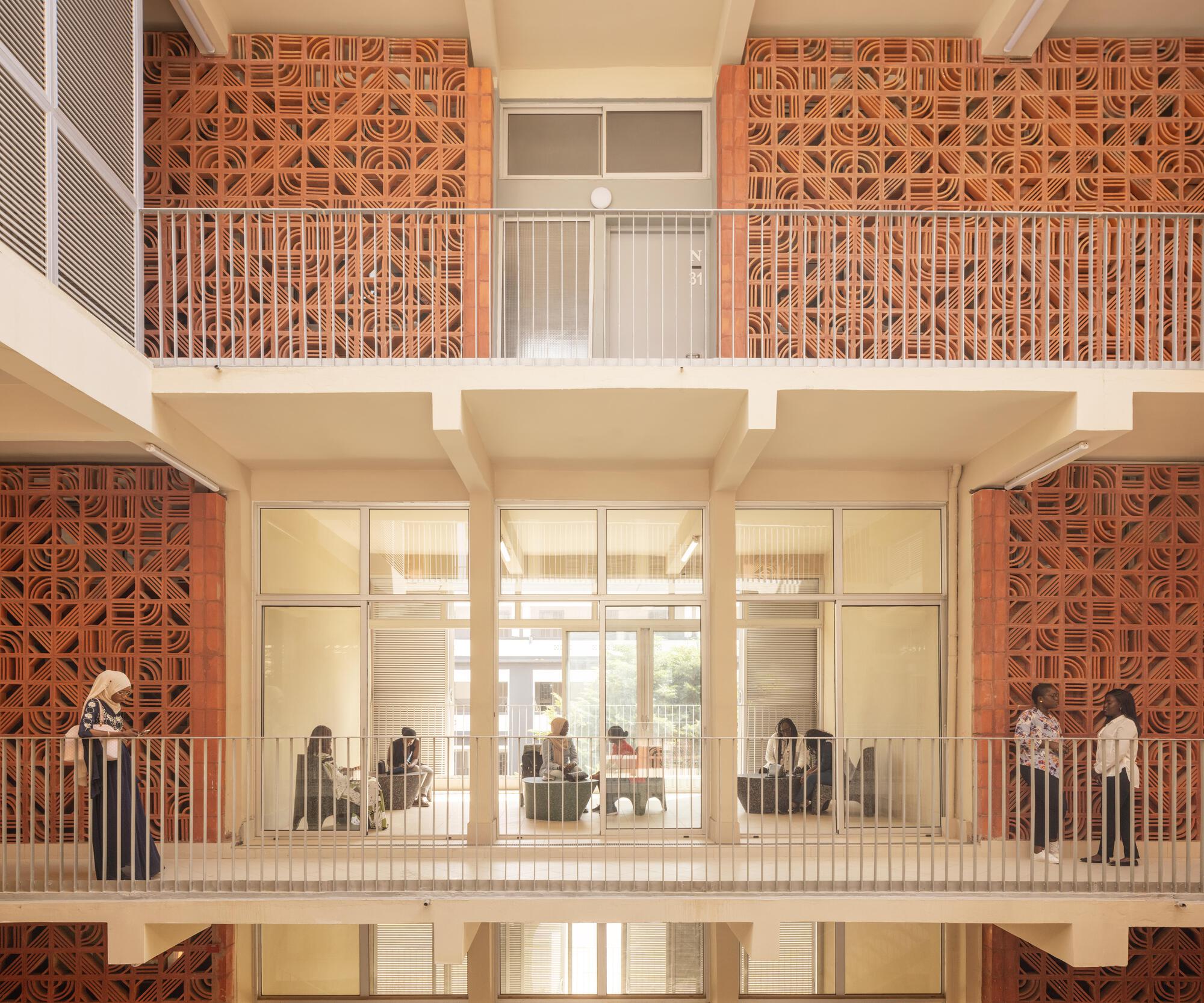 Courtyard elevation of stacked walkways with terracotta screens and metal railings, students standing on the balcony and sitting in the glazed room