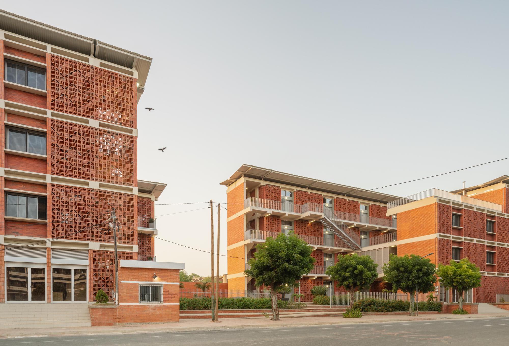 Corner view of perforated brick screens and an exterior steel stair, with two birds flying overhead in warm evening light