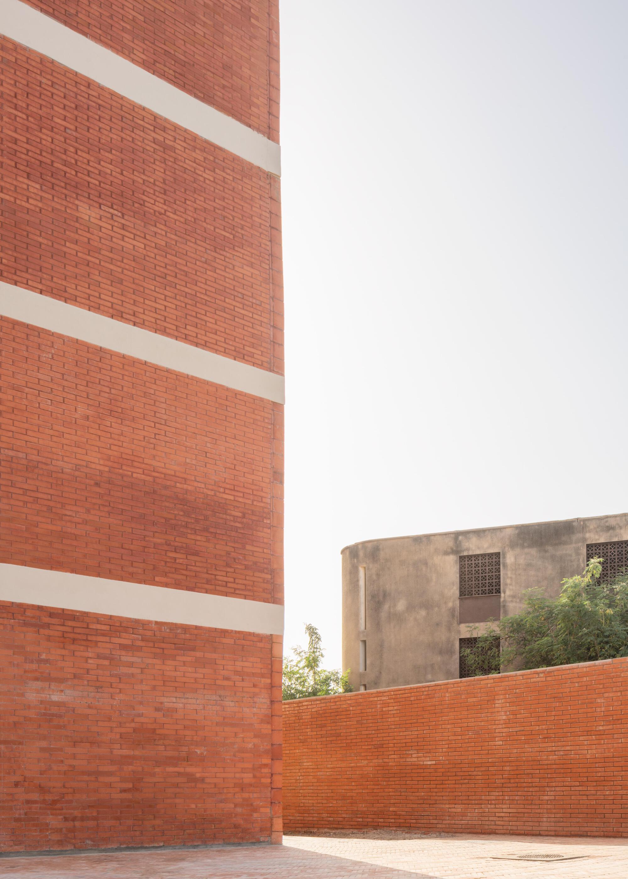Close view of a red brick wall with pale concrete bands beside a low brick wall, a weathered concrete block behind in hazy light