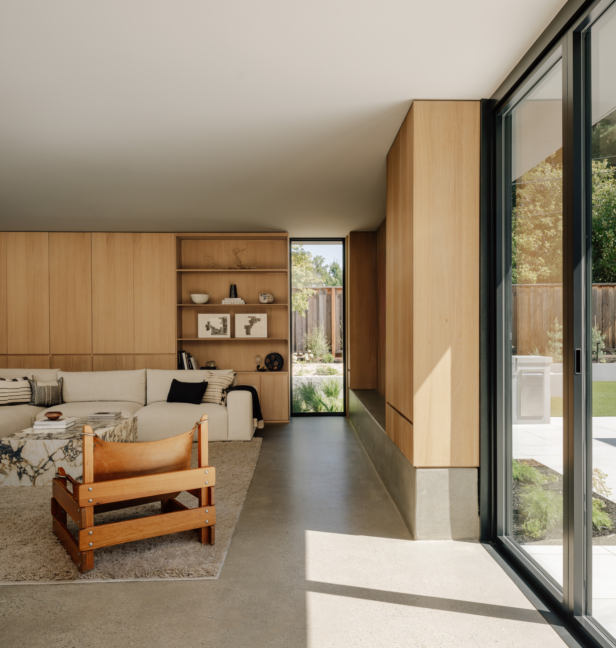 Living room with oak cabinetry, a leather sling chair and a tall narrow window, sunlight falling across the concrete floor