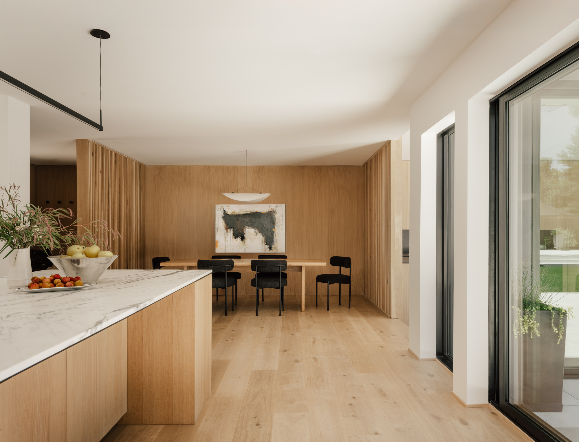 Open dining area with oak slatted walls, a marble-topped island in the foreground and a sliding glass door at right