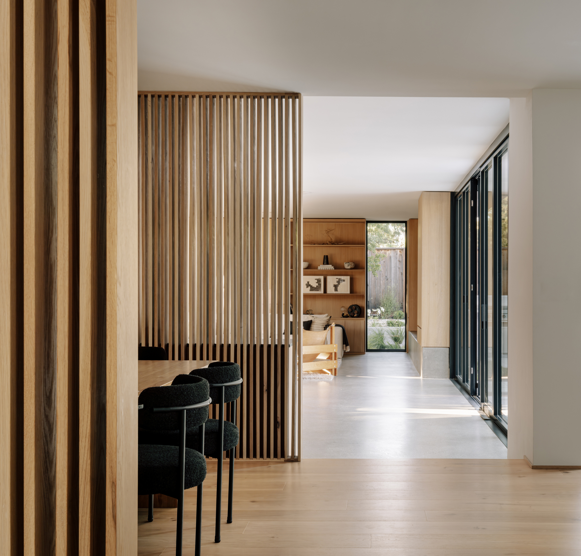 View through an oak slat partition from the dining area toward a shelved living room and glazed garden wall