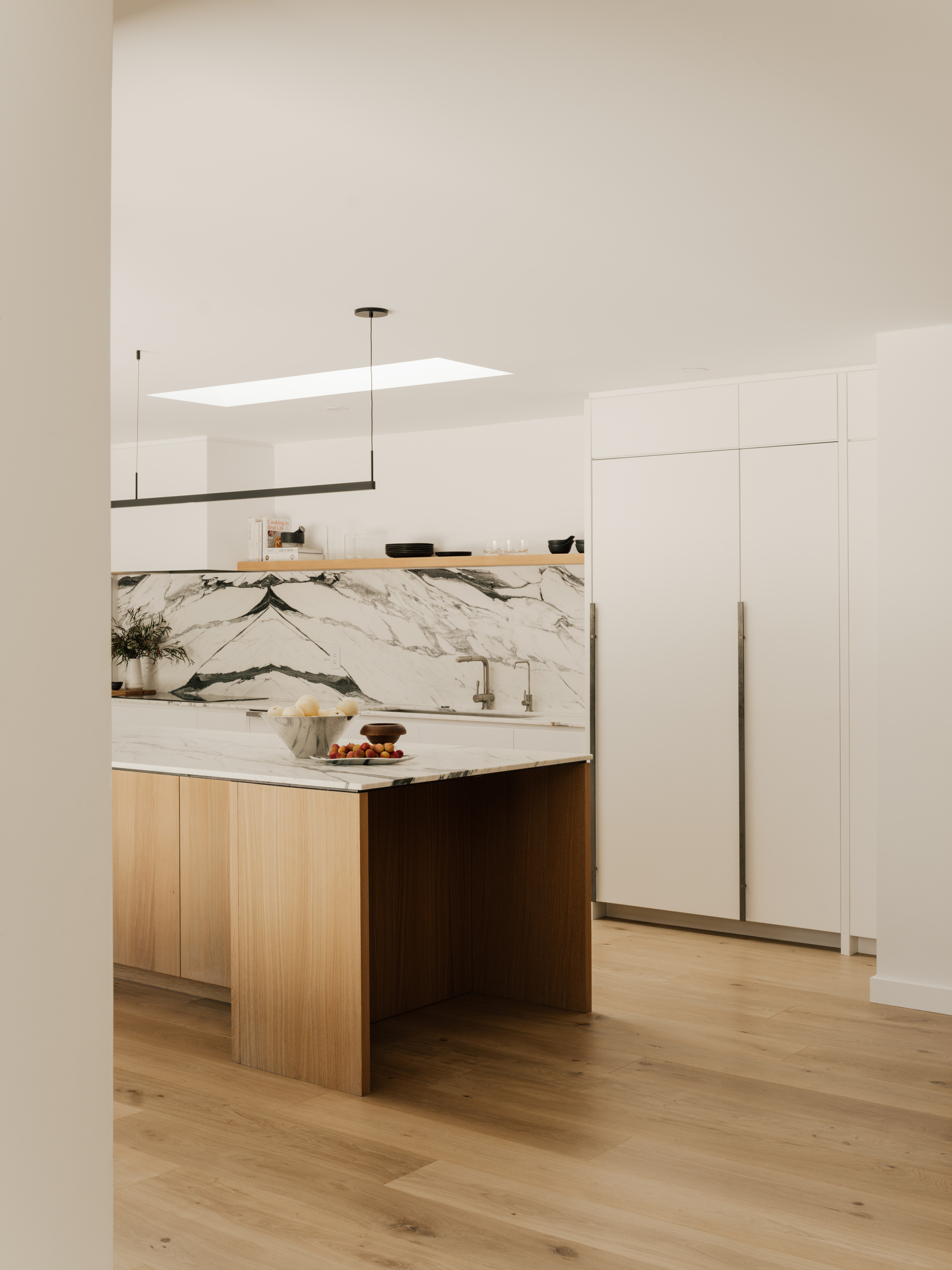 Kitchen island clad in oak beside a veined marble backsplash, with a skylight washing daylight over the ceiling