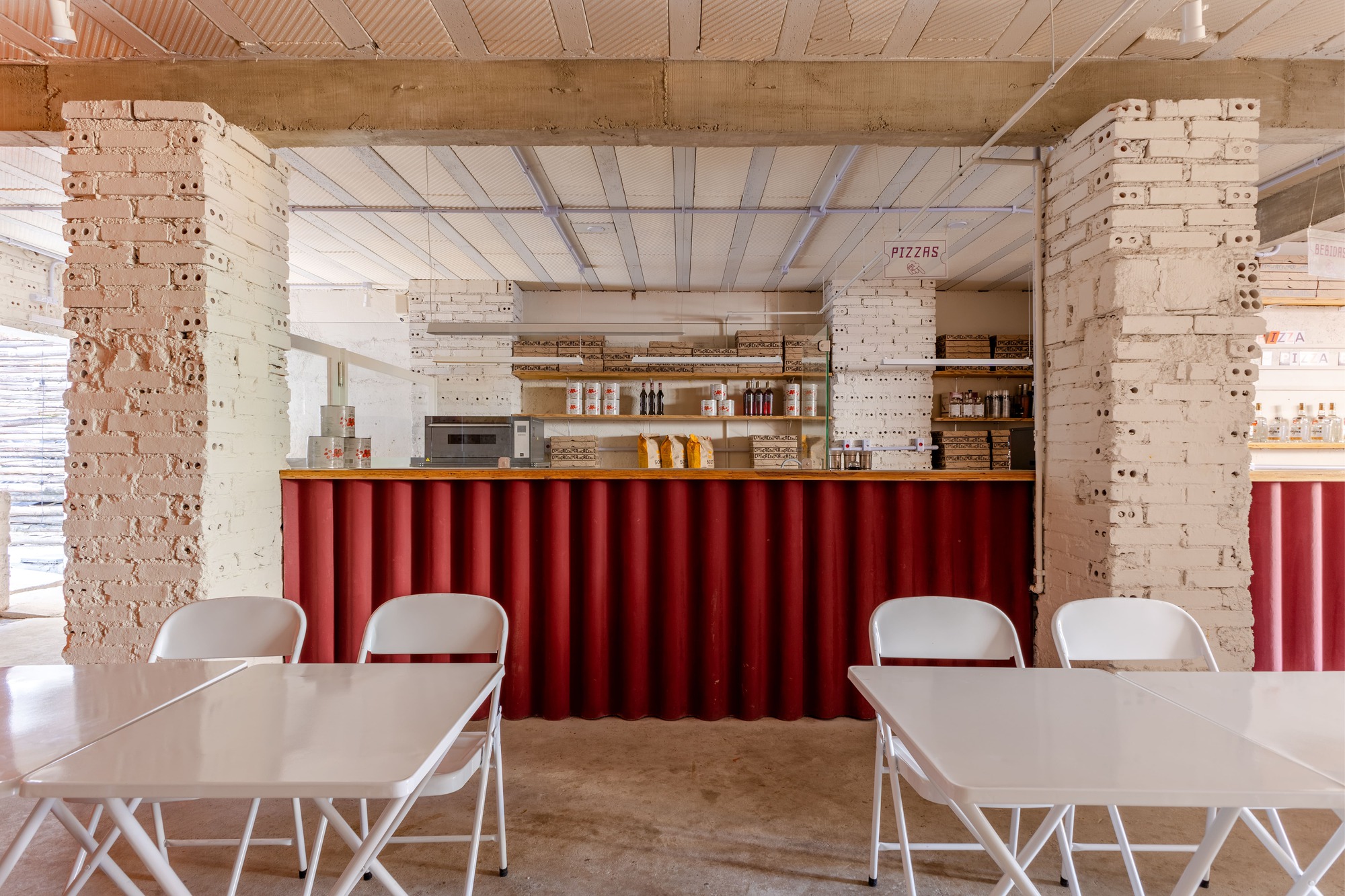 Red corrugated service counter between two painted white brick pillars, with folding white tables and chairs in the foreground