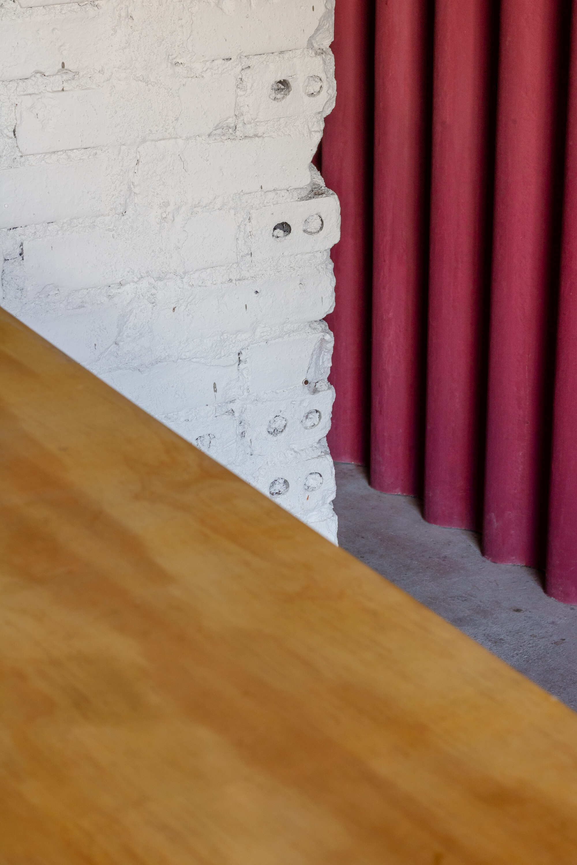 Corner of a painted white brick wall with hollow holes beside a maroon corrugated panel, with a plywood tabletop edge in the foreground