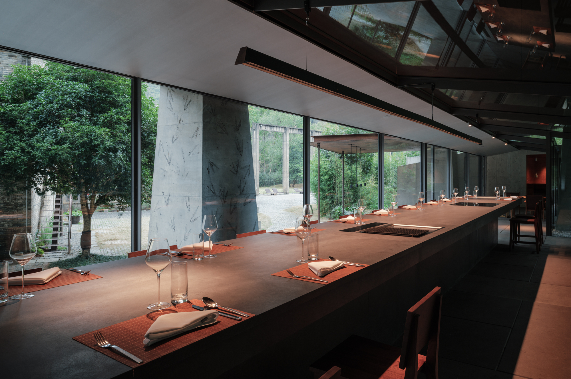 Counter set with folded napkins and wine glasses beside a leaf-imprinted concrete wall and a courtyard tree in daylight