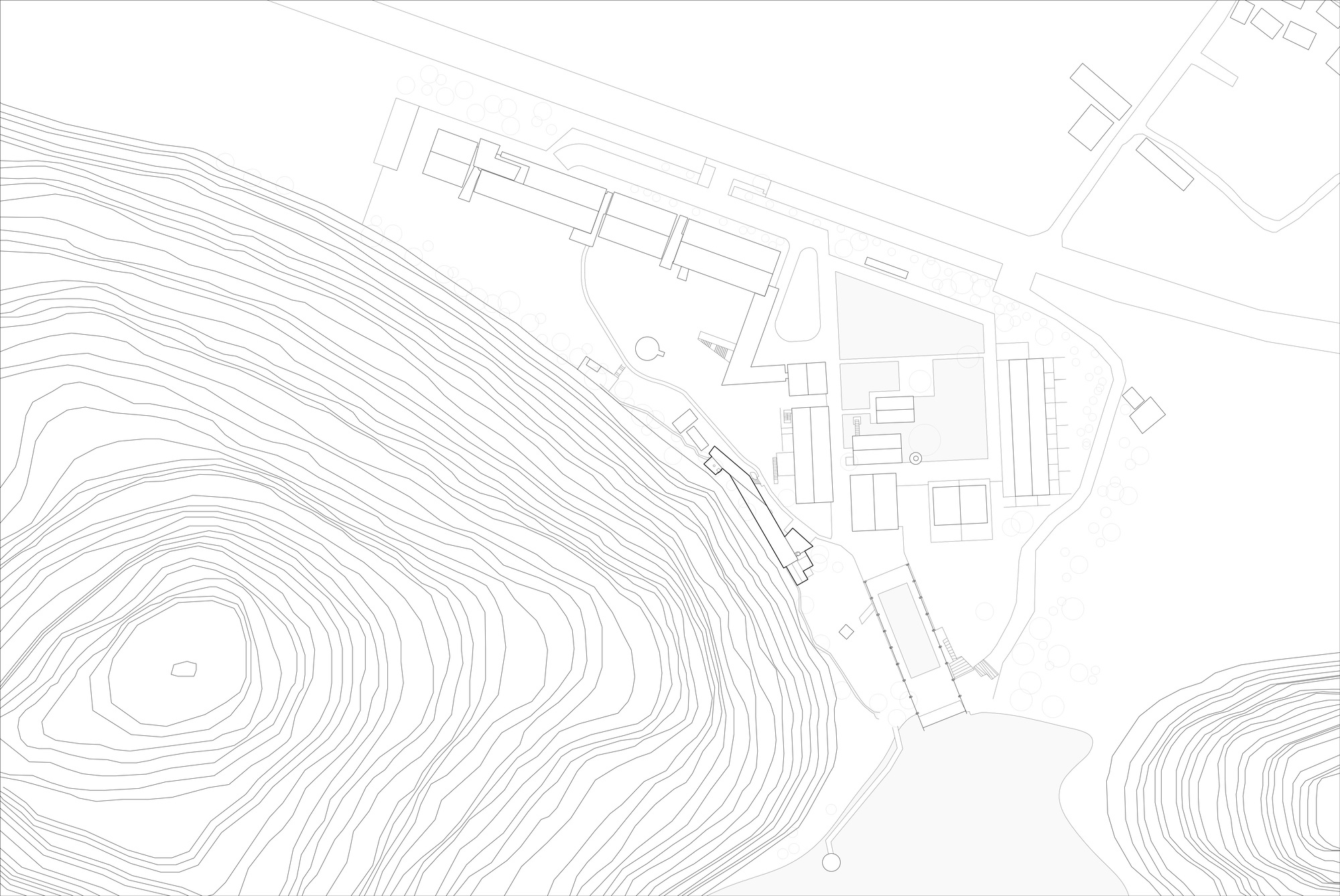 Site plan drawing showing a long narrow building along contour lines of a hillside, beside clustered buildings and a road