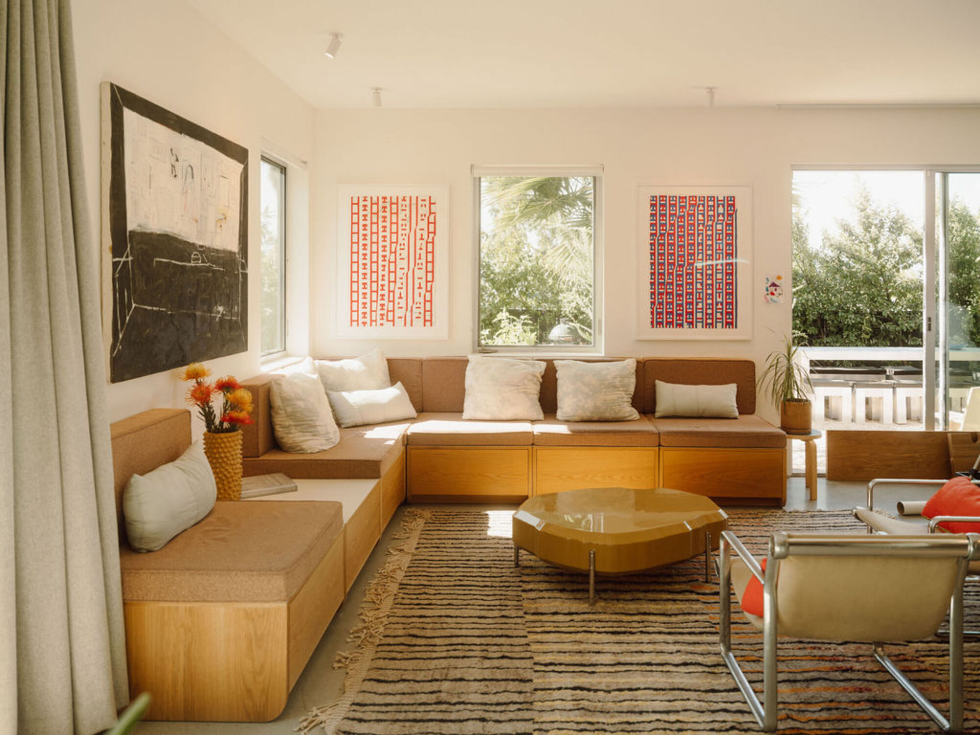 Living room corner with a built-in oak bench sofa, framed prints and a low gold table under afternoon light