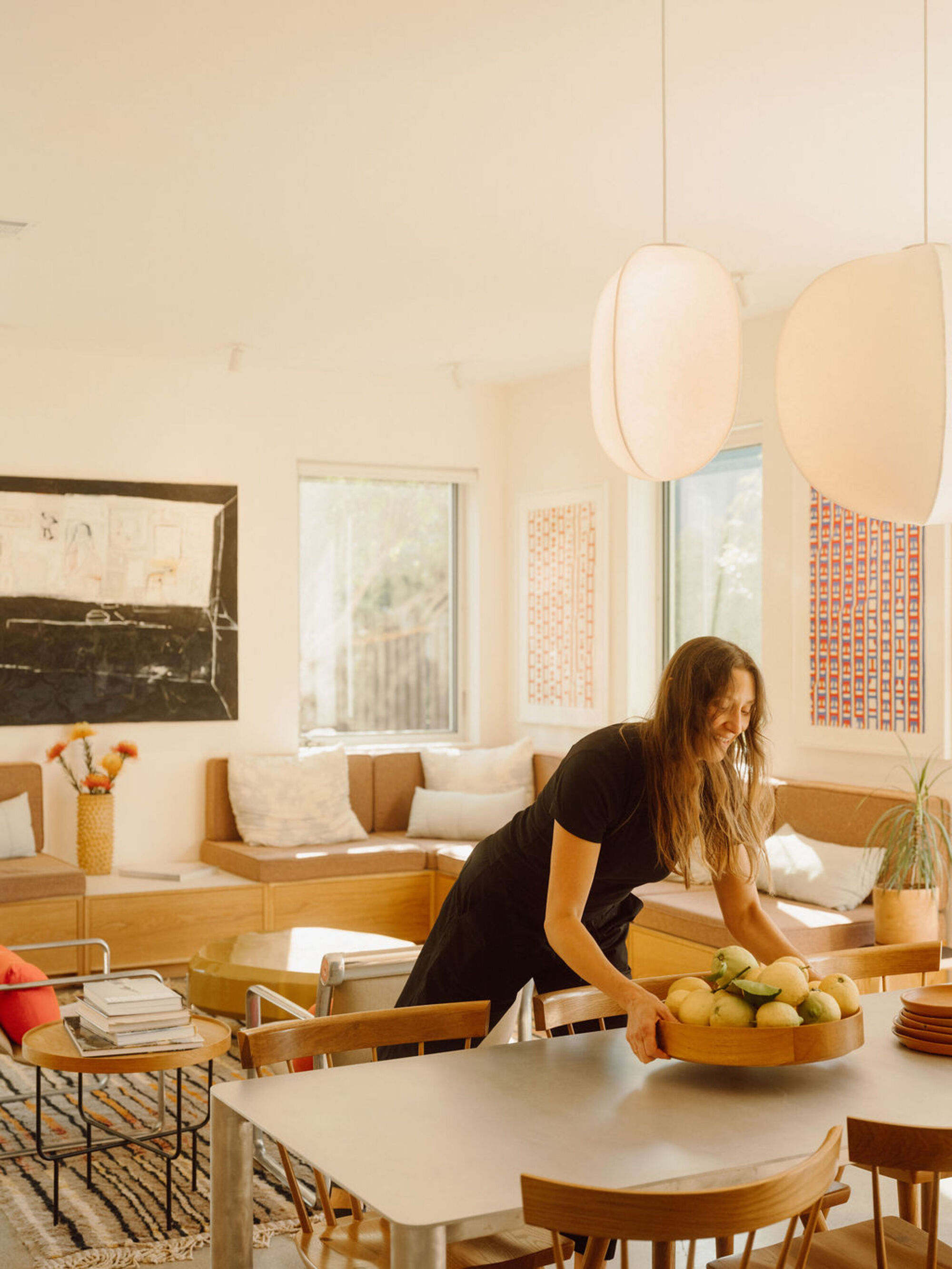 Woman setting a bowl of fruit on the dining table, with the bench seating and pendant lamps behind her